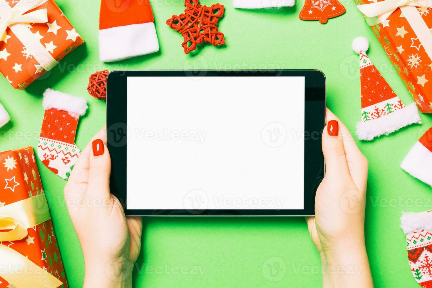 Top view of woman holding tablet in her hands on green background made of Christmas decorations. New Year holiday concept. Mockup photo