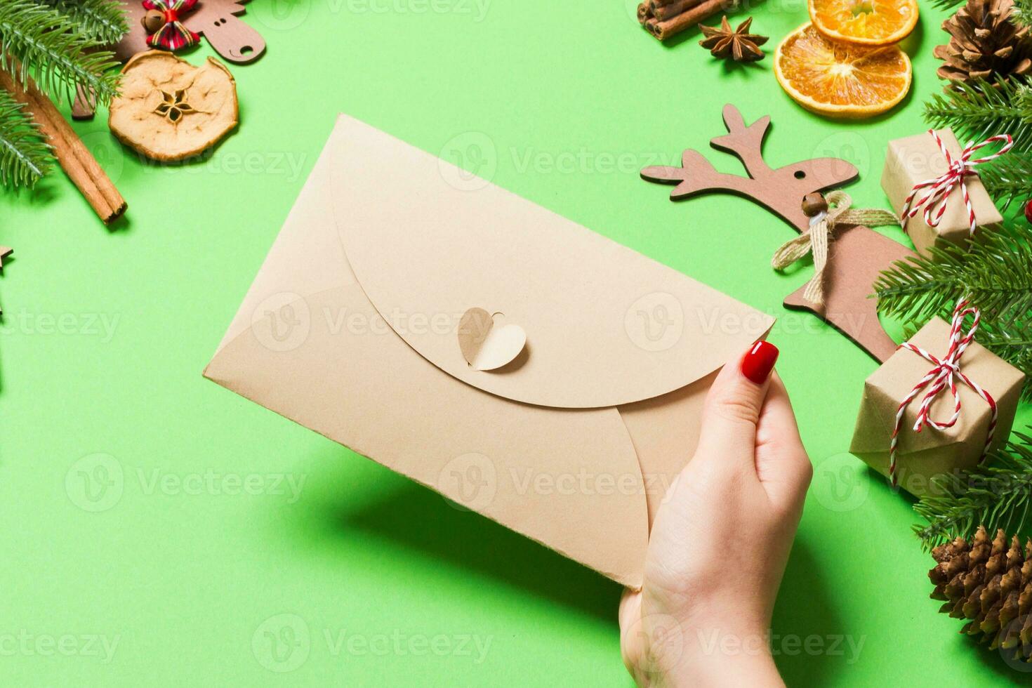 vista superior de una mujer sosteniendo un sobre sobre fondo verde hecho de decoraciones navideñas. concepto de tiempo de navidad foto