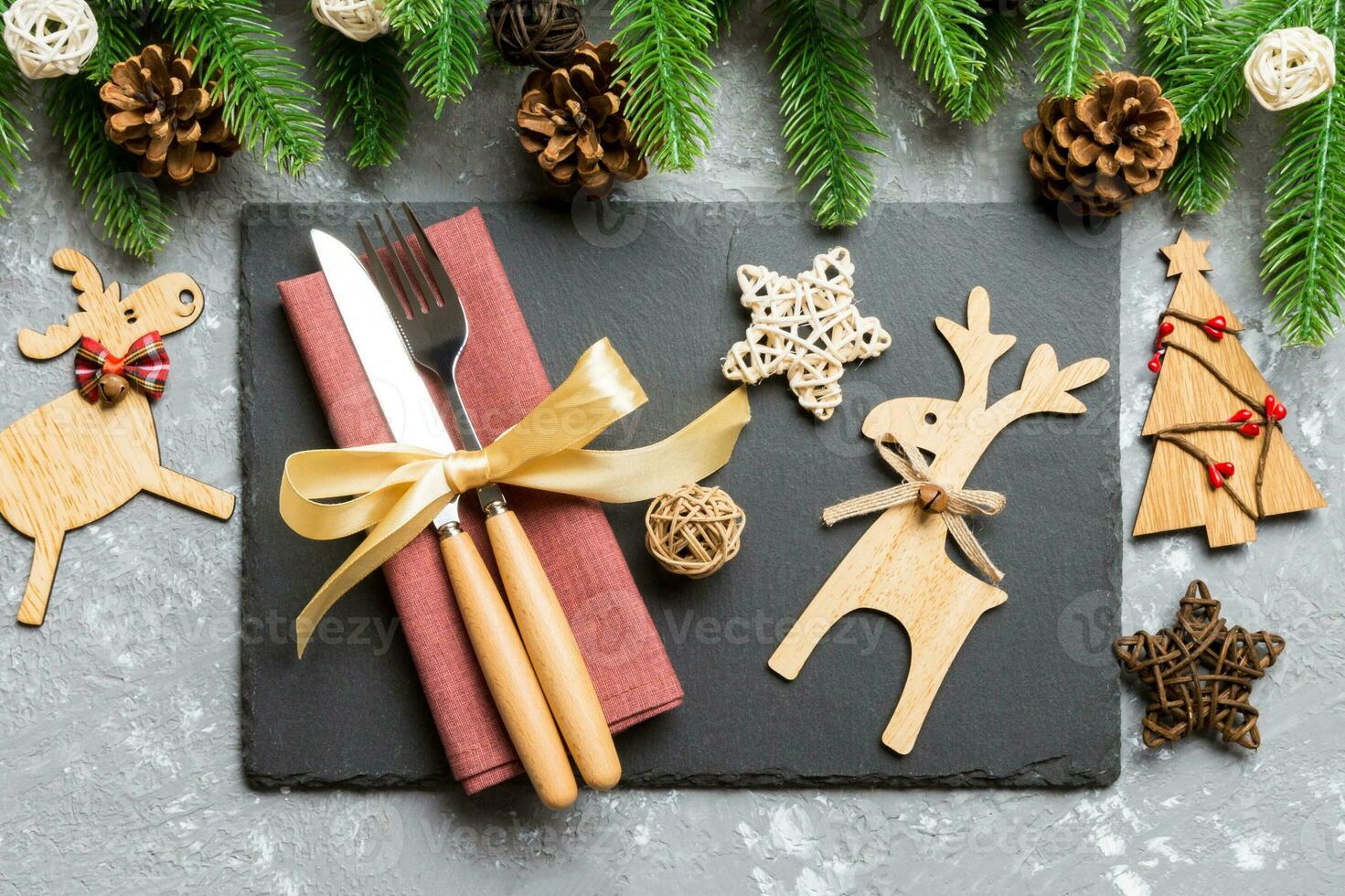 Top view of New Year dinner on festive cement background. Composition of plate, fork, knife, fir tree and decorations. Merry Christmas concept photo