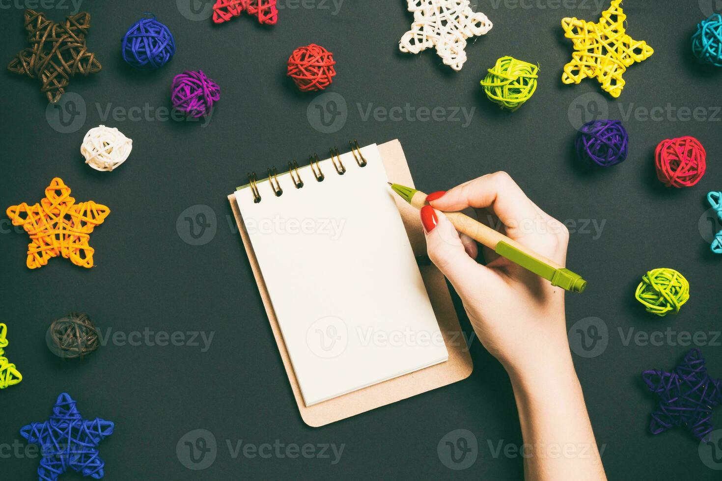 Top view of female hand making some notes in noteebok on colorful background. New Year decorations and toys. Christmas time concept photo