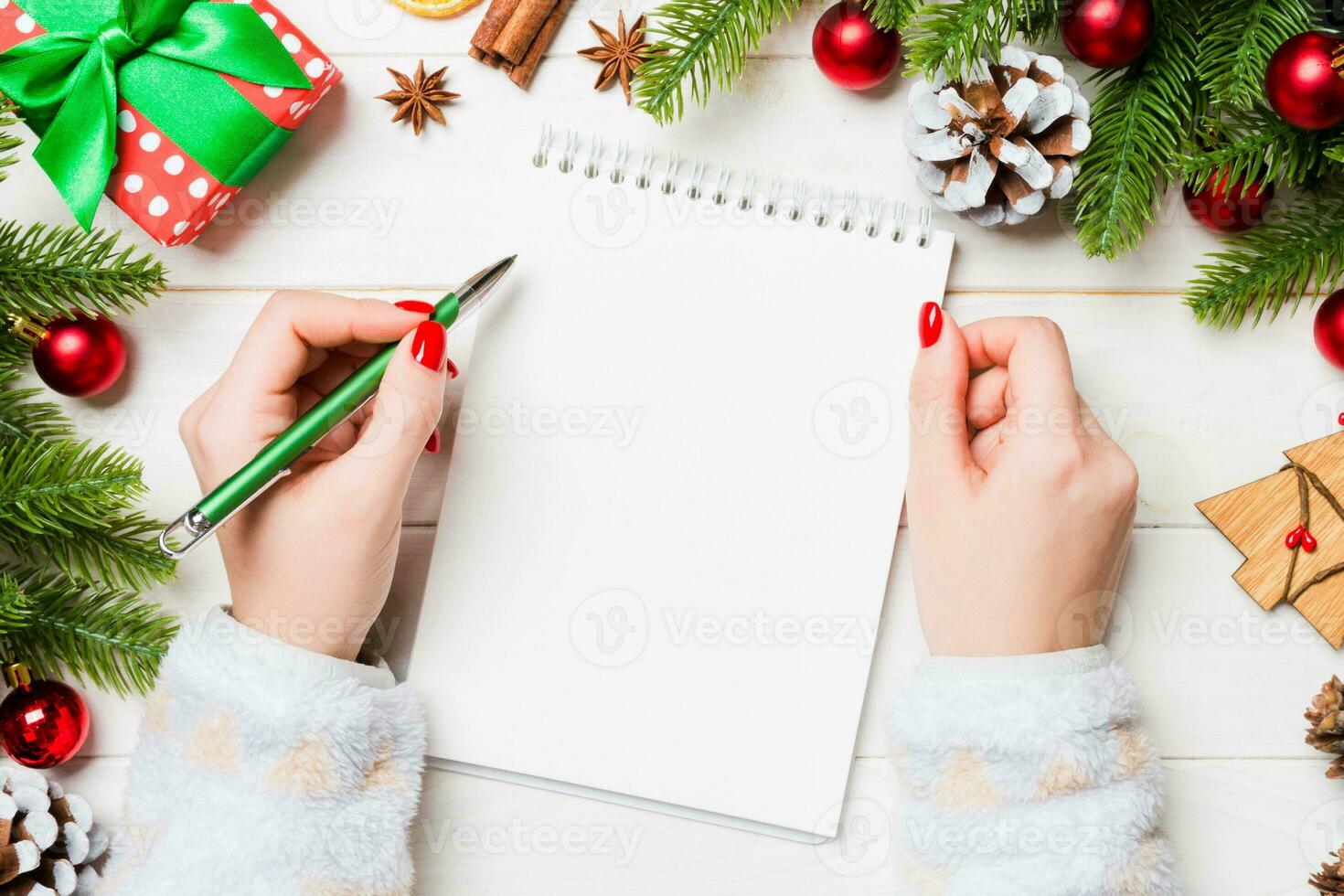 Top view of female hand writing in a notebook on wooden Christmas background. Fir tree and festive decorations. Wish list. New Year concept photo