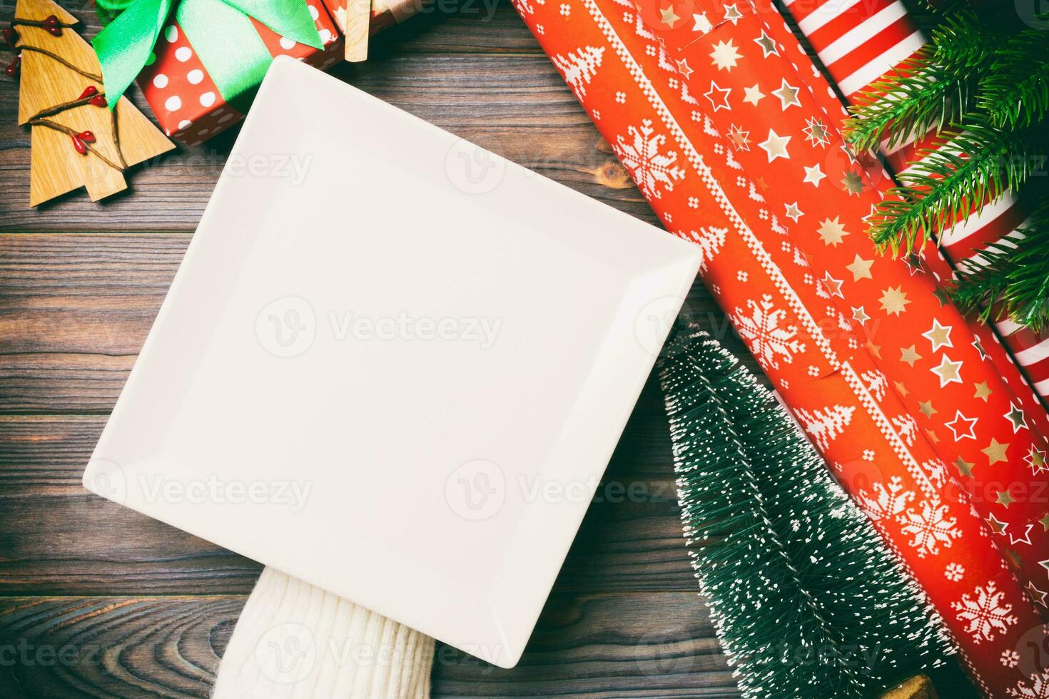 Top view of female hand holding a plate on holiday wooden background. Fir tree and Christmas decorations. New Year time cocnept photo