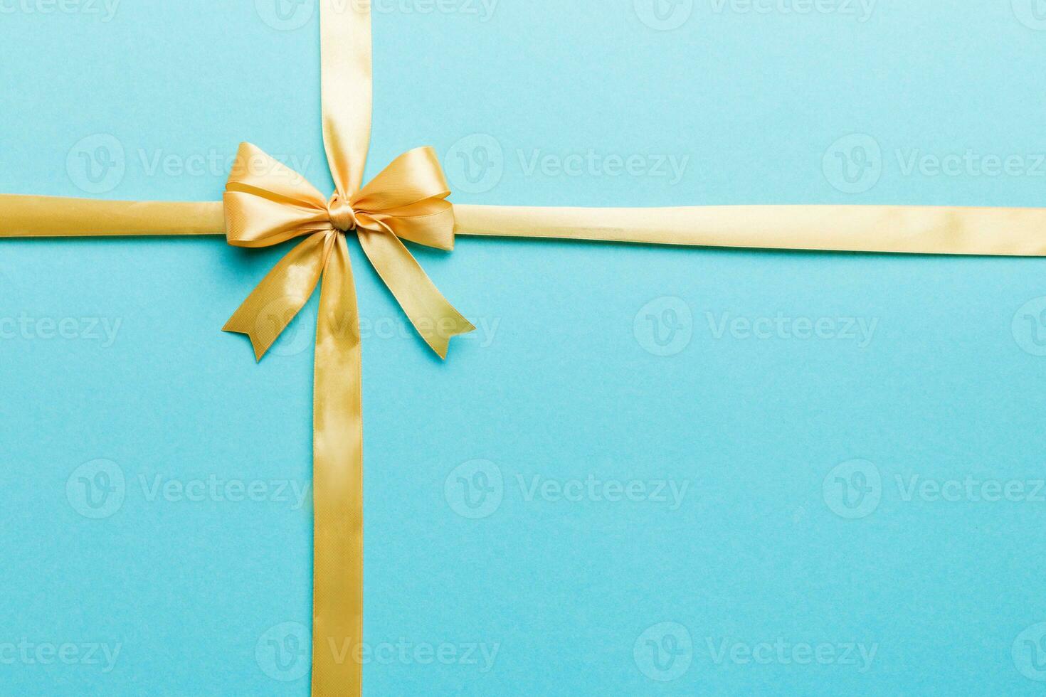 Top view of gold ribbon rolled and yellowbow isolated on colored background. Flat lay with copy space photo