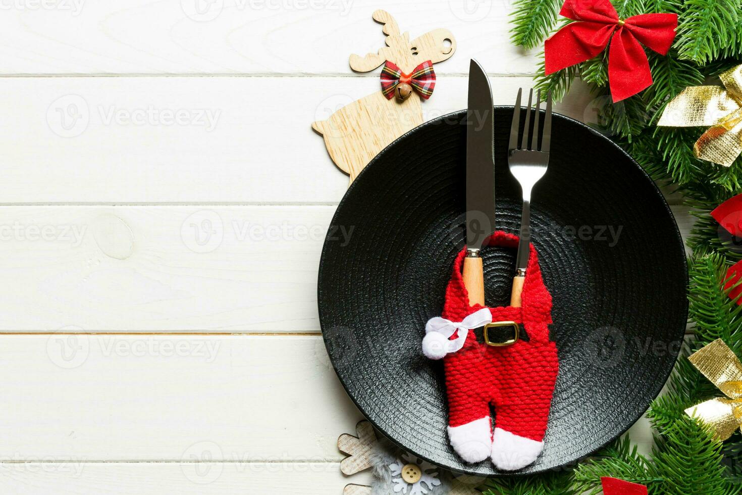 Top view of Christmas dinner on wooden background. Plate, utensil, fir tree and holiday decorations with copy space. New Year time concept photo