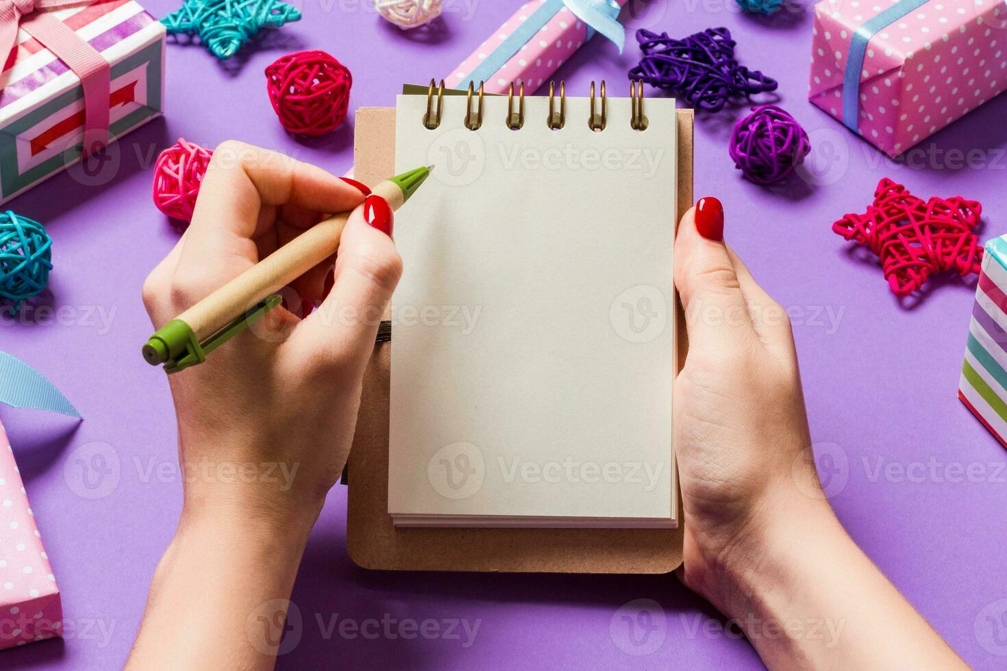 Top view of female hand making some notes in noteebok on purple background. New Year decorations and toys. Christmas time concept photo