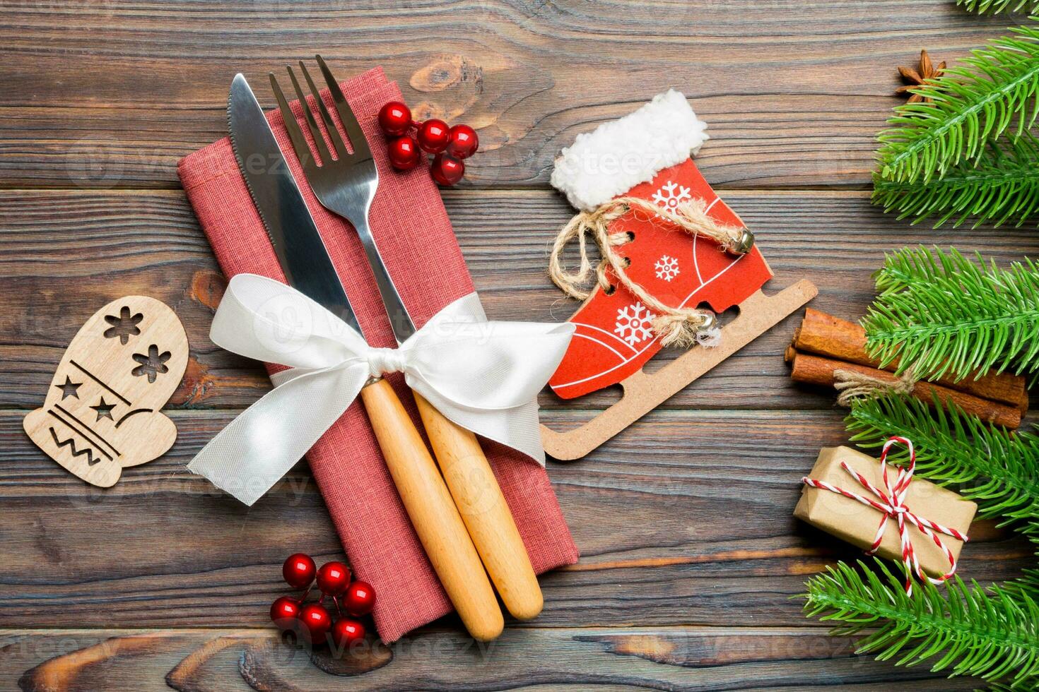 Top view of christmas decorations on wooden background. Close up of fork and knife on napkin tied up with ribbon. New year pattern concept photo