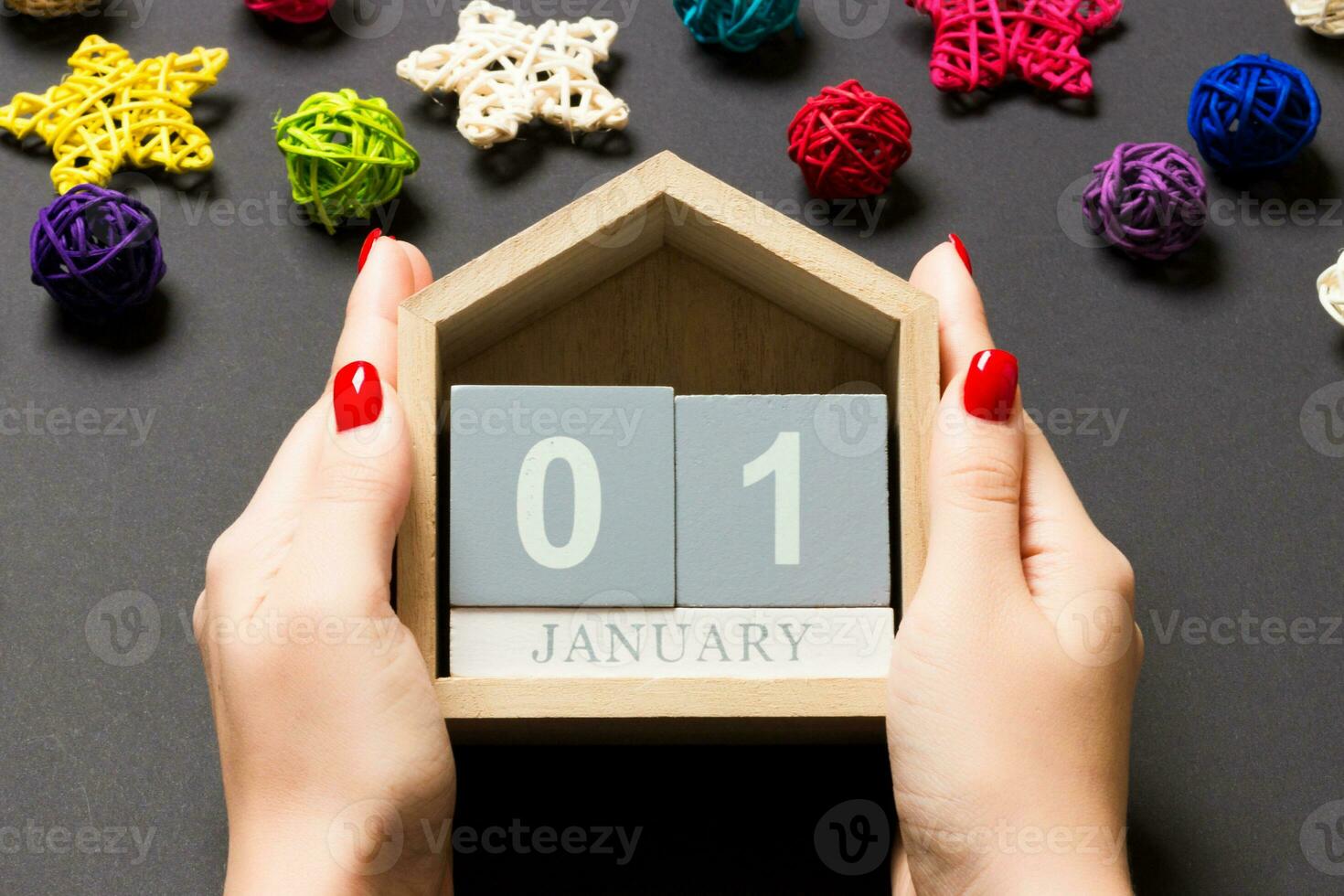 Top view of female hands holding calendar on black background. The first of January. Holiday decorations. New Year concept photo