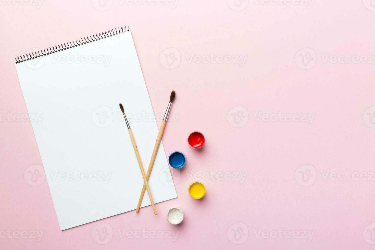 Album pages and paints, pencils, brush on a colored background. Top view with empty space. workplace for creativity. home teaching concept drawing photo