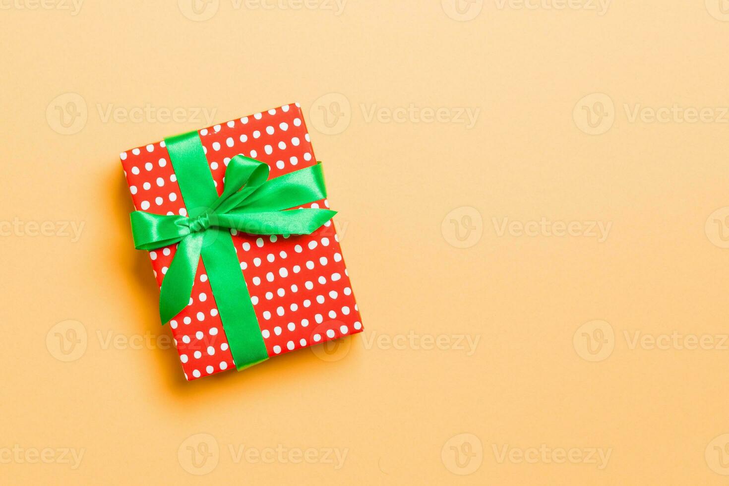 Gift box with green bow for Christmas or New Year day on orange background, top view with copy space photo