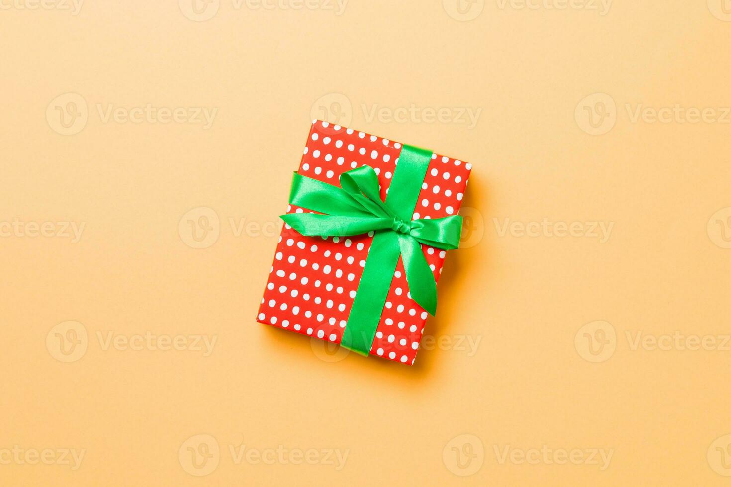 Gift box with green bow for Christmas or New Year day on orange background, top view with copy space photo