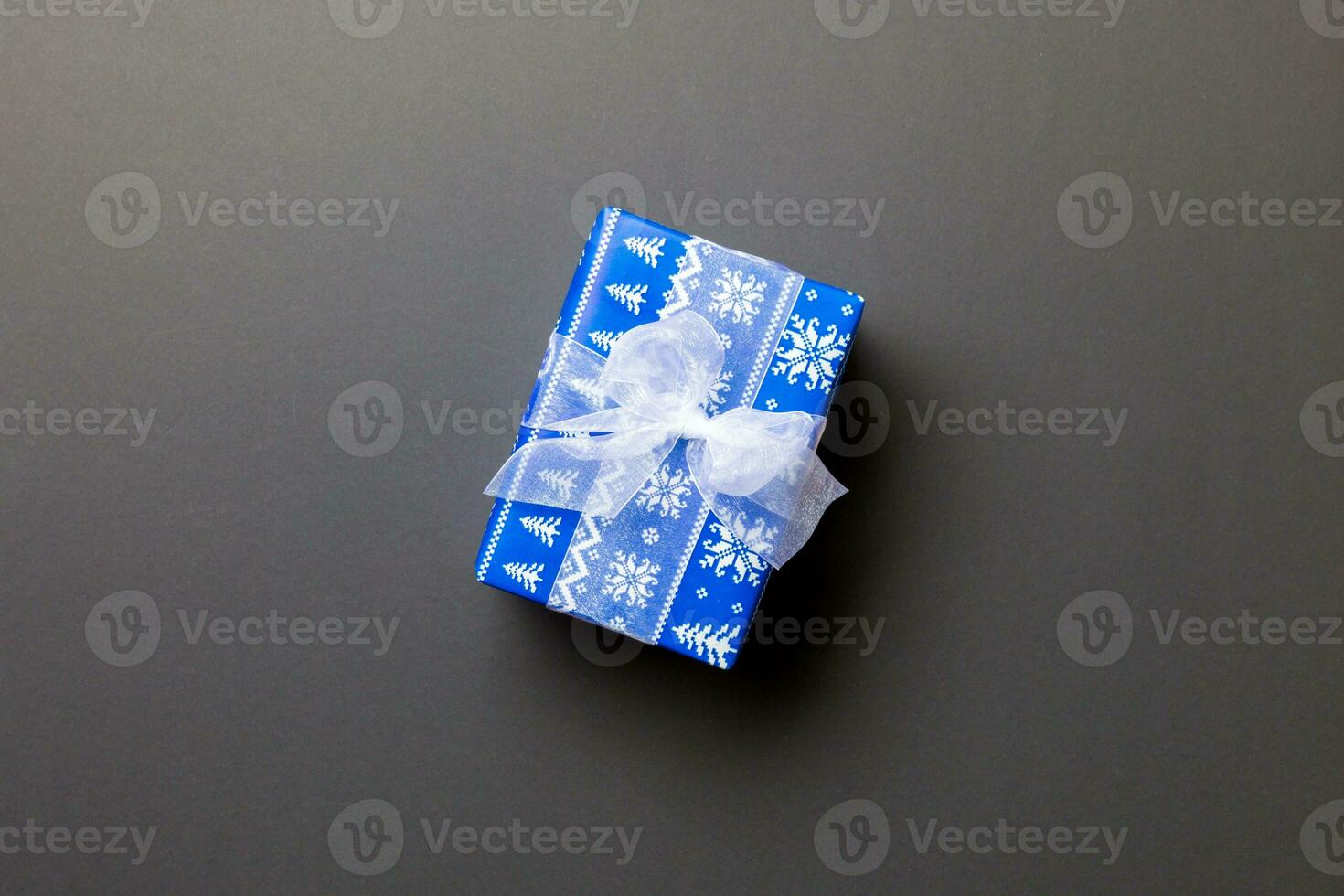 wrapped Christmas or other holiday handmade present in paper with white ribbon on black background. Present box, decoration of gift on colored table, top view with copy space photo