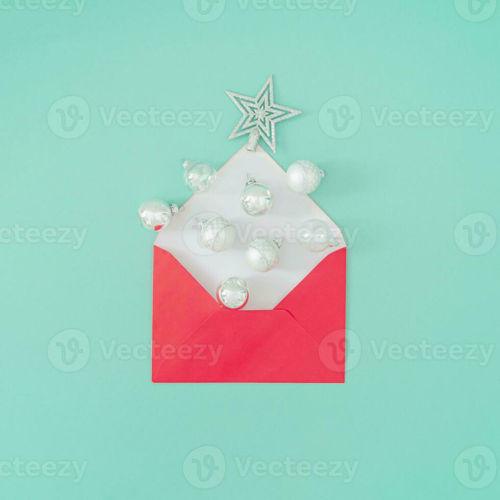 Creative composition made of Christmas baubles coming out of red envelope on pastel green background. Minimal Christmas or New Year concept. Trendy winter holidays idea. Flat lay, top of view. photo