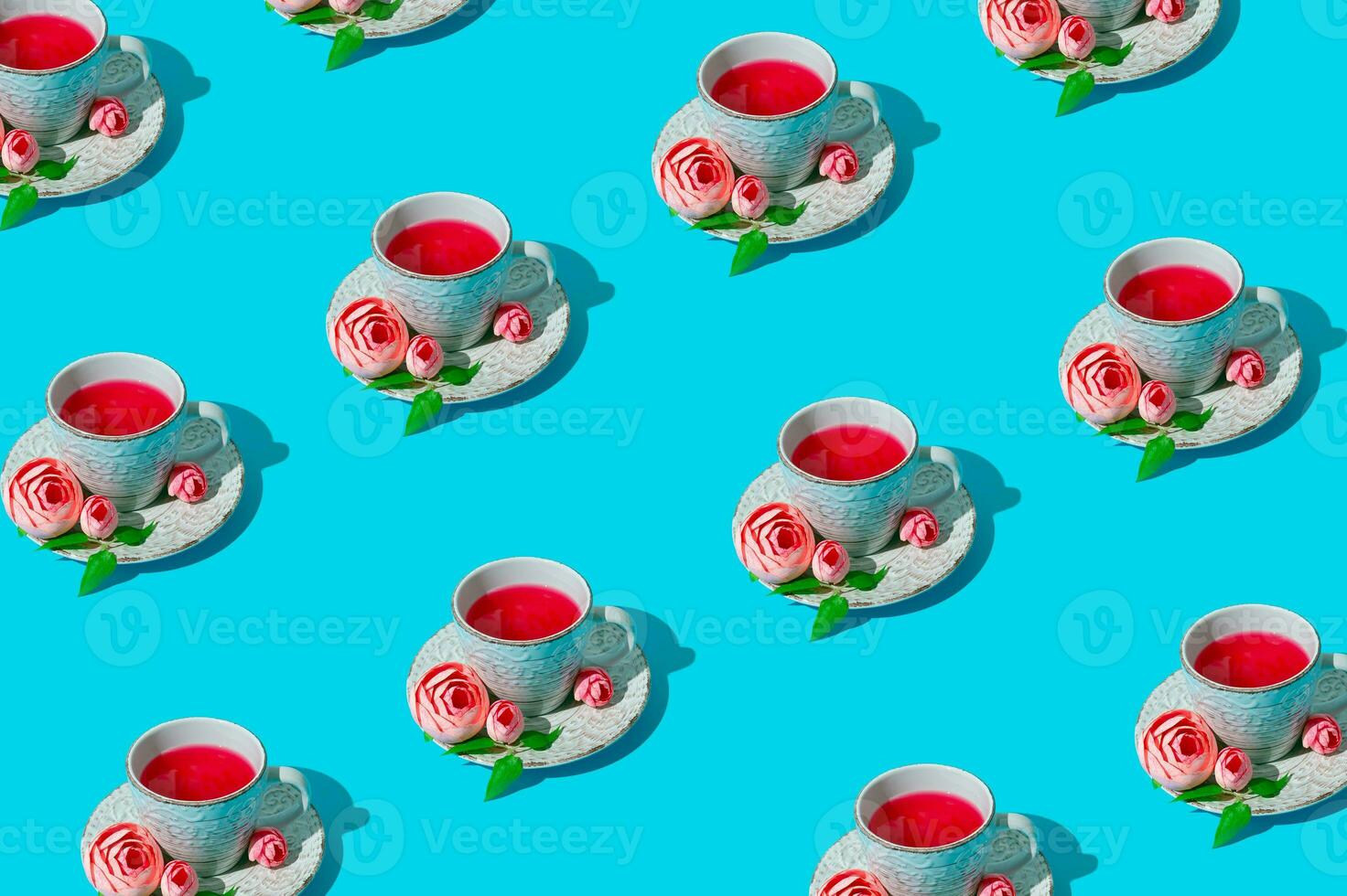Creative trendy pattern made of cup of tea decorated with pink flowers and green leaves on bright light blue background. Minimal hot drink and flowers concept. Fancy floral tea composition. photo