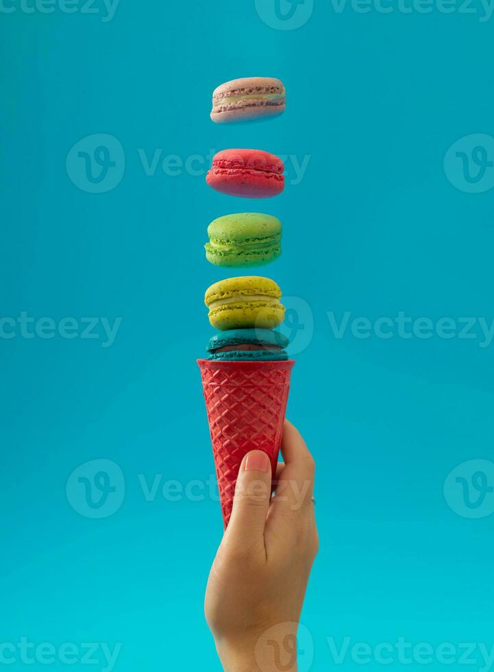 Pink waffle ice cream cone with colorful macarons on bright blue background. Minimal food concept. Sweet creative idea. Yummy macaron cookies and ice cream layout. photo