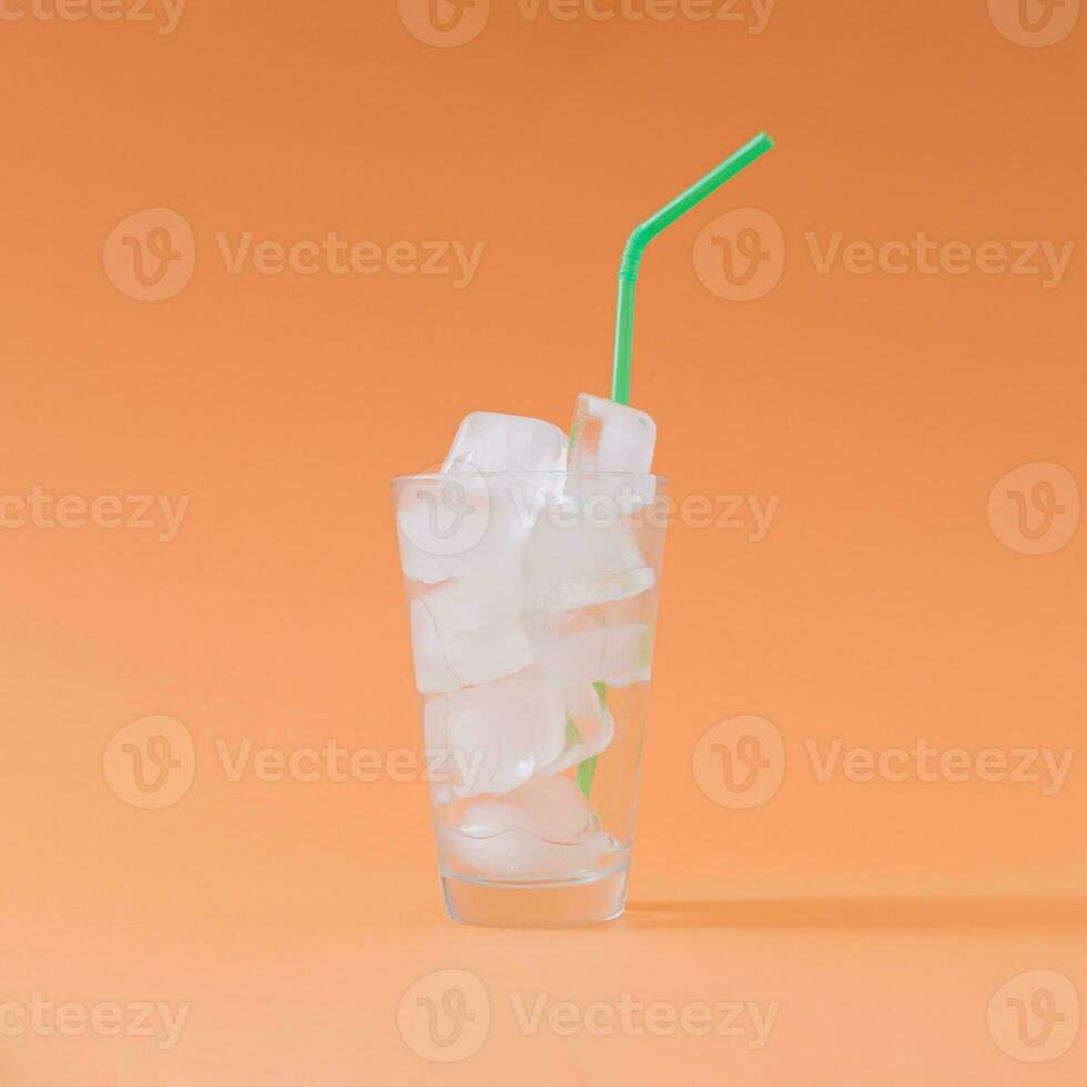 Creative composition made of empty glass full of ice cubes with green drinking straw on pastel orange background. Minimal diet no calories concept. Be healthy lifestyle idea. photo
