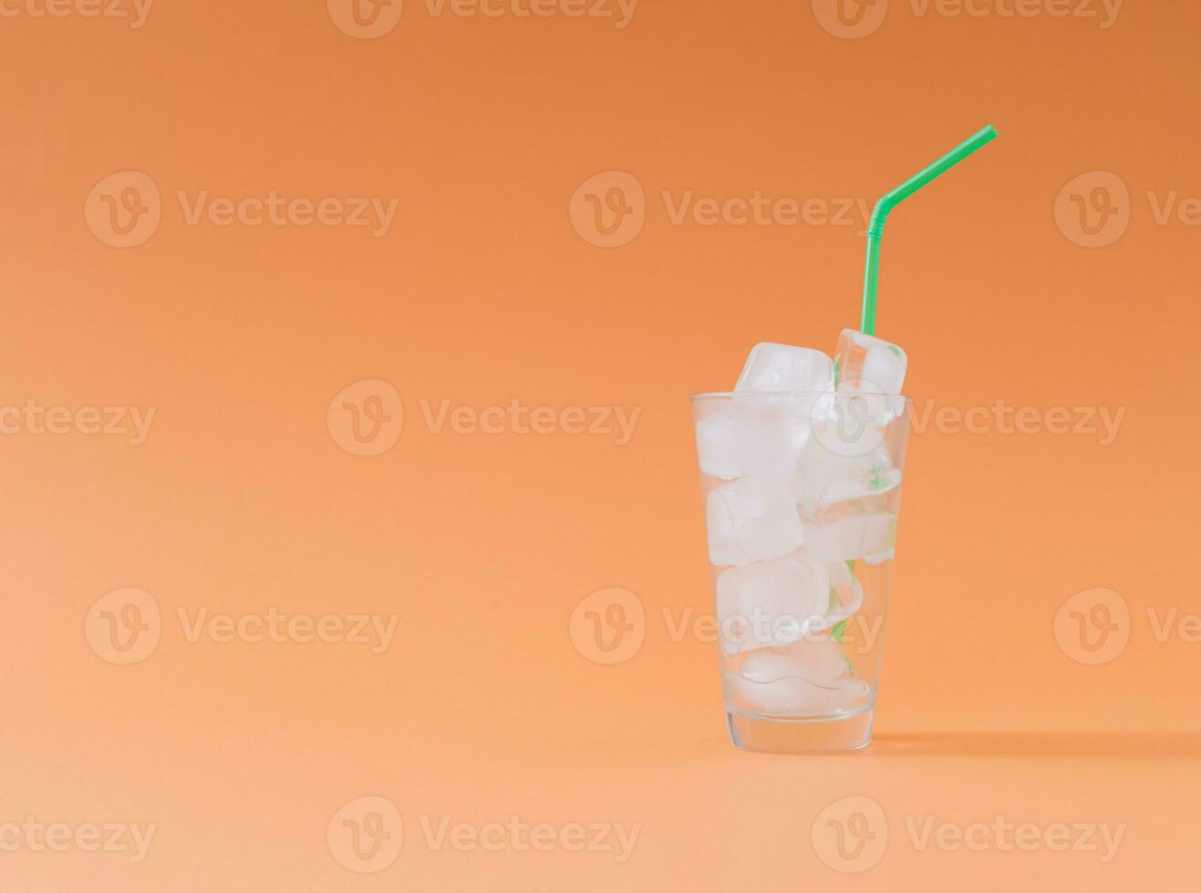 Creative composition made of empty glass full of ice cubes with green drinking straw on pastel orange background. Minimal diet no calories concept. Be healthy lifestyle idea. Copy space. photo