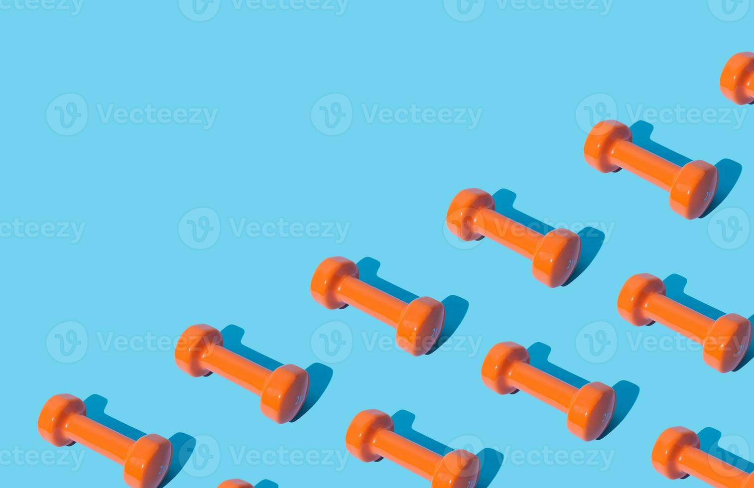 Creative pattern composition made of orange dumbbells on light blue background with copy space. Minimal fitness, healthy lifestyle and sport concept. Trendy exercise and fitness backround idea. photo