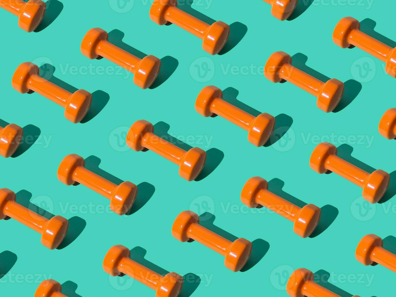 Creative pattern composition made of orange dumbbells on pastel green background. Minimal fitness, healthy lifestyle and sport concept. Trendy exercise and fitness backround idea. photo
