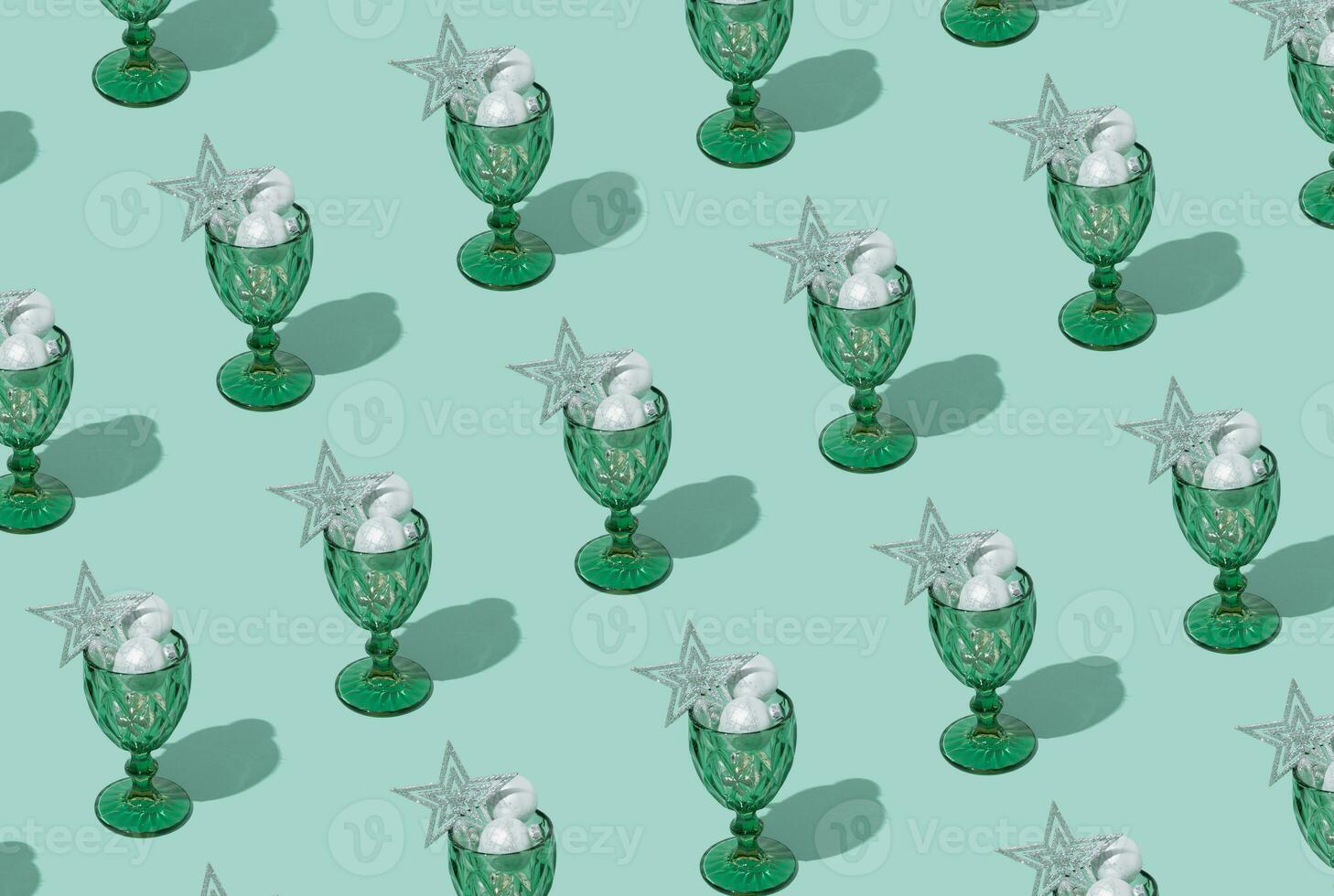 Pattern made of Christmas baubles cocktail decoration in wine glass on pastel green background. New year or Christmas eve party concept. photo