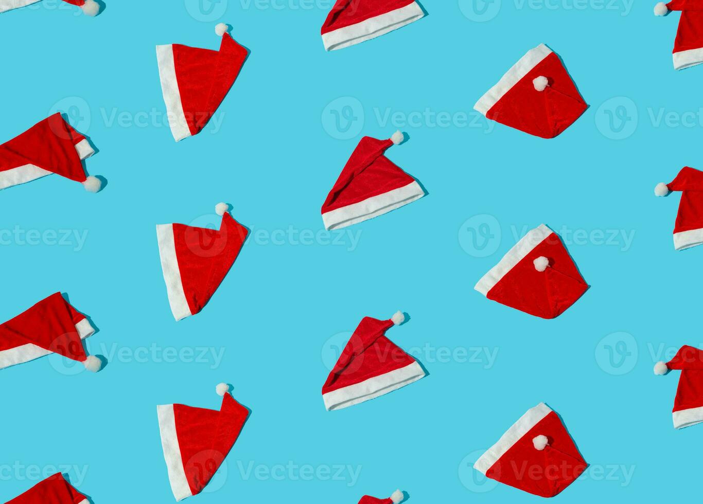 Trendy Christmas pattern made with Santa Claus hats on bright light blue background. Minimal Christmas or New Year concept. Creative flat lay composition. Winter holidays idea. photo