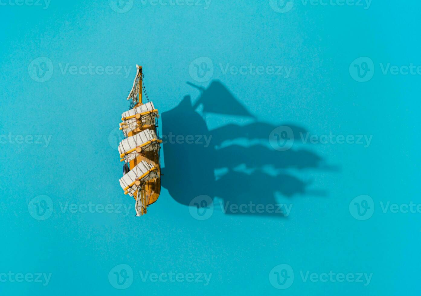 Old ship traveling on the sea. Sailing boat and shadow on blue background composition. Travel, vacation and summer journey concept. Flat lay summer sailboat and shadow idea. Copy space. photo