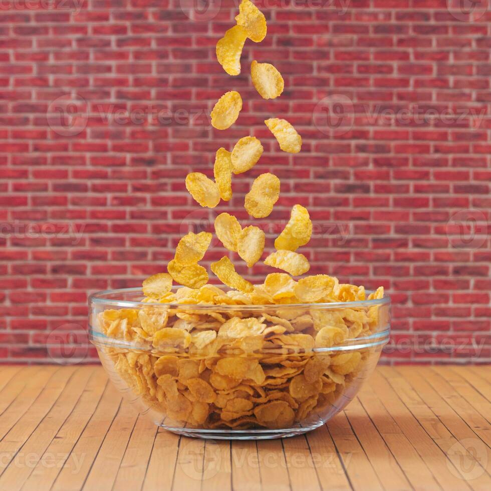 Creative layout made of healthy corn flakes falling into glass bowl against red brick wall background. Minimal breakfast food concept. Fancy breakfast cereal idea. Cornflakes aesthetic. photo