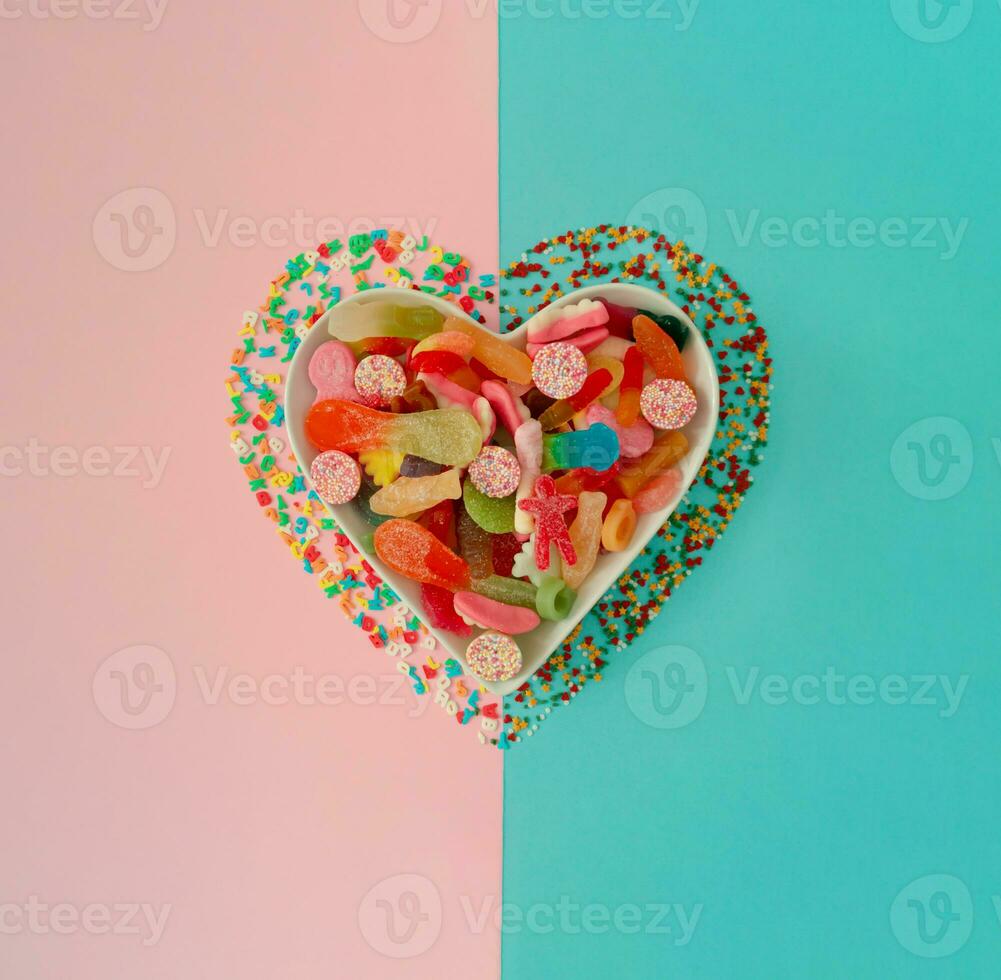 Creative heart made of gummy candies and sprinkles on pastel pink and blue background. Trendy love concept. Flat lay aesthetic. photo