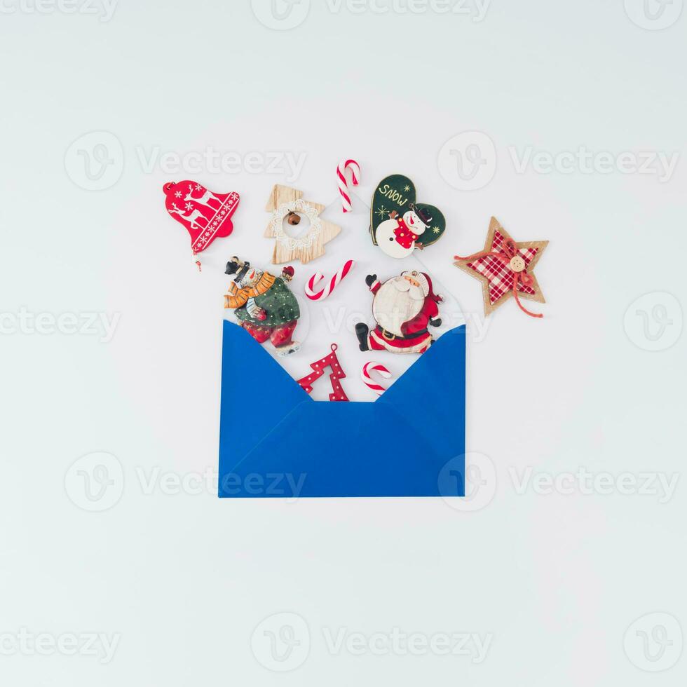 Creative composition made of various Christmas objects coming out of blue envelope on white background. Minimal Christmas or New Year concept. Trendy winter holidays idea. Flat lay, top of view. photo