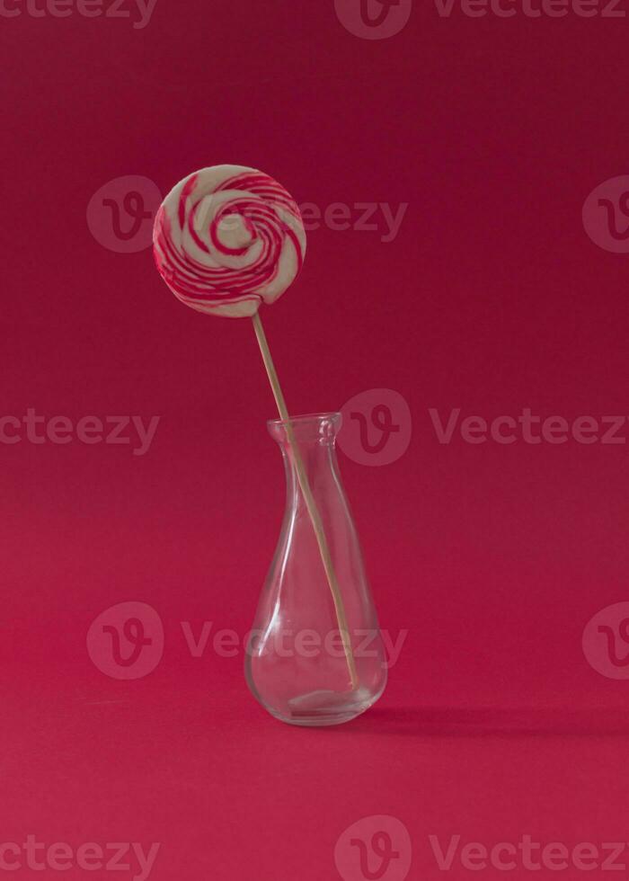 Lollipop as a flower in a vase against red background. Summer candy concept. Creative sweet idea. photo