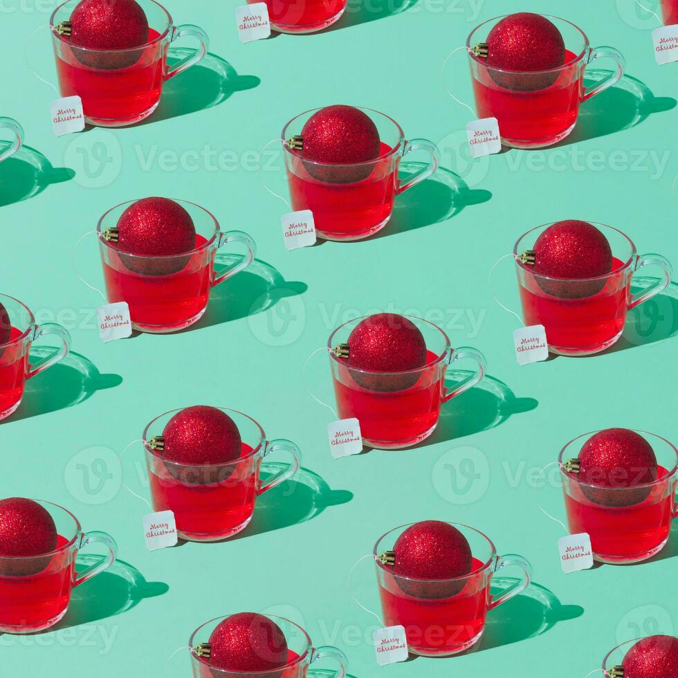 Christmas pattern composition of transparent glass cup of fruit tea with teabag made of red Christmas bauble on green background. Minimal Christmas or New Year concept. Trendy winter holidays idea. photo