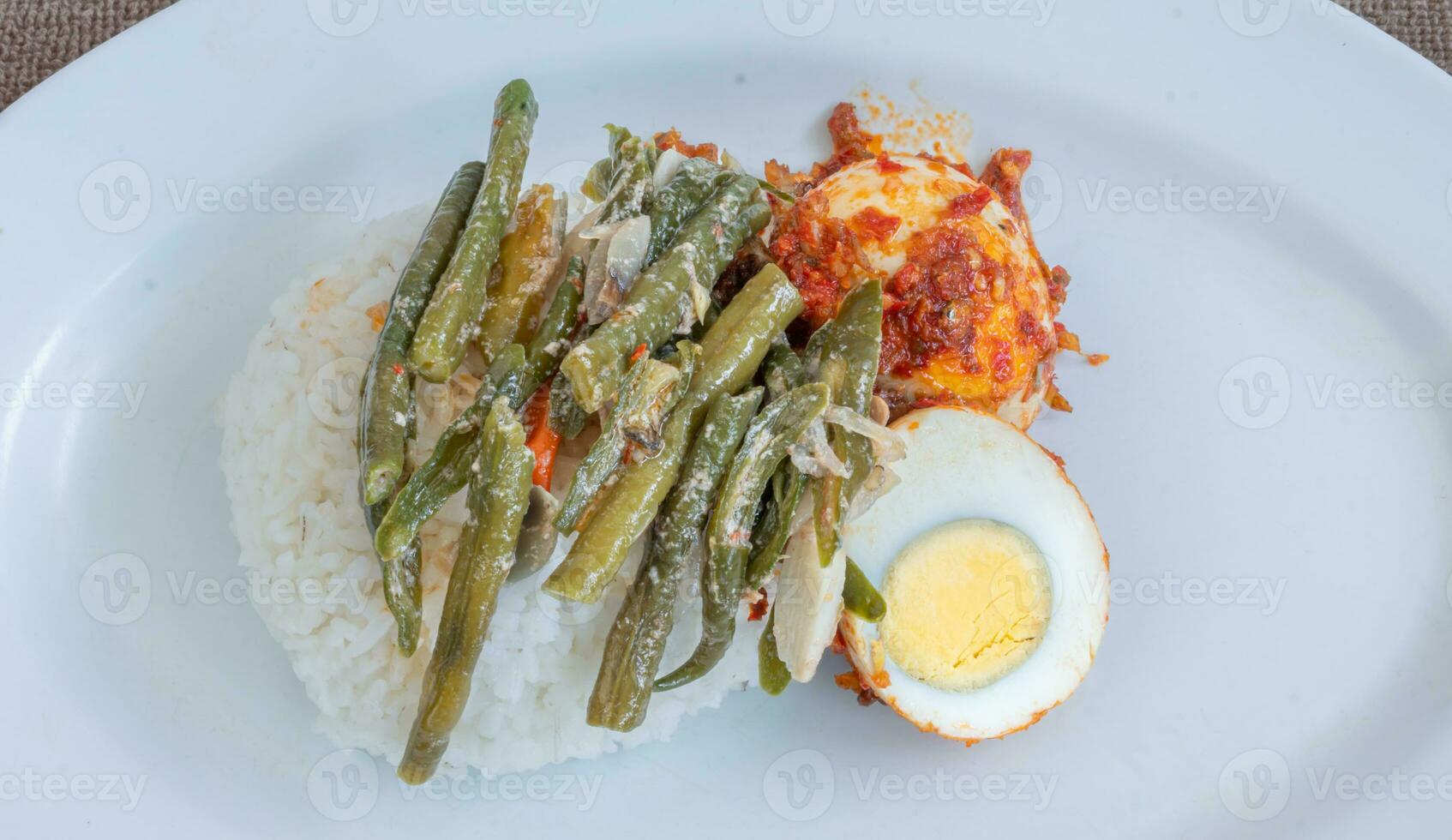 A plate of rice with egg balado and long bean sauce, chili sauce filled with eggs, anchovies and tofu. Served in a bowl on a gray background. Selected focus. photo