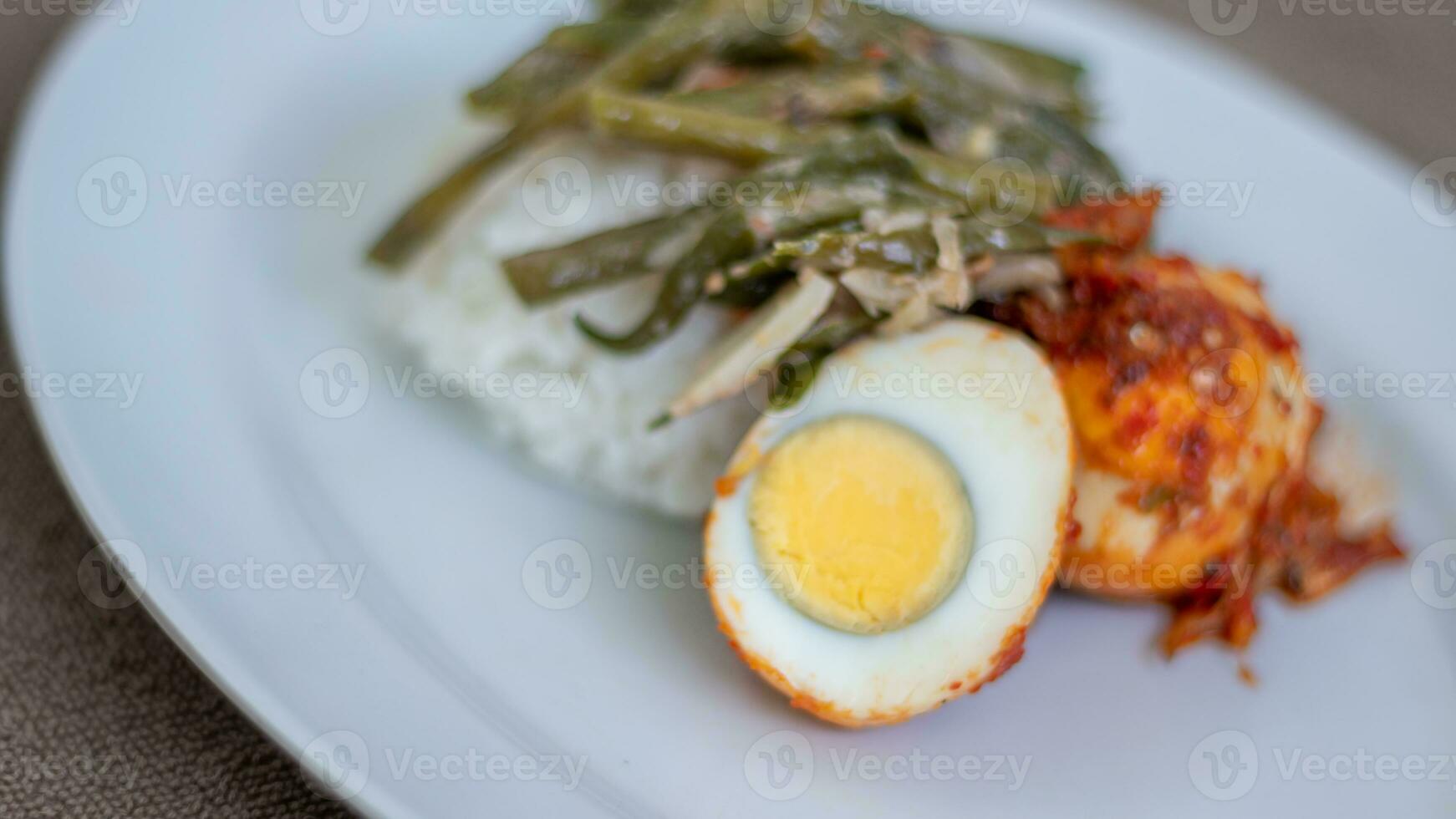 A plate of rice with egg balado and long bean sauce, chili sauce filled with eggs, anchovies and tofu. Served in a bowl on a gray background. Selected focus. photo