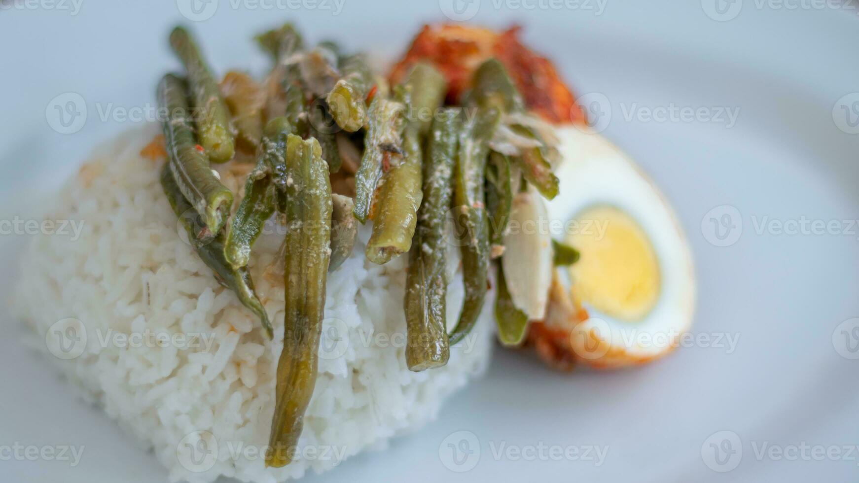 A plate of rice with egg balado and long bean sauce, chili sauce filled with eggs, anchovies and tofu. Served in a bowl on a gray background. Selected focus. photo