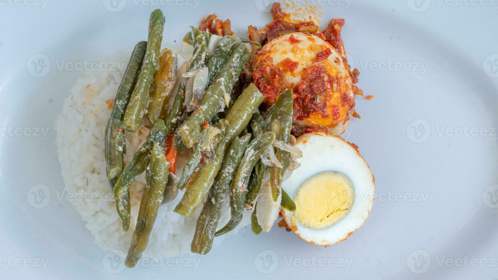 A plate of rice with egg balado and long bean sauce, chili sauce filled with eggs, anchovies and tofu. Served in a bowl on a gray background. Selected focus. photo