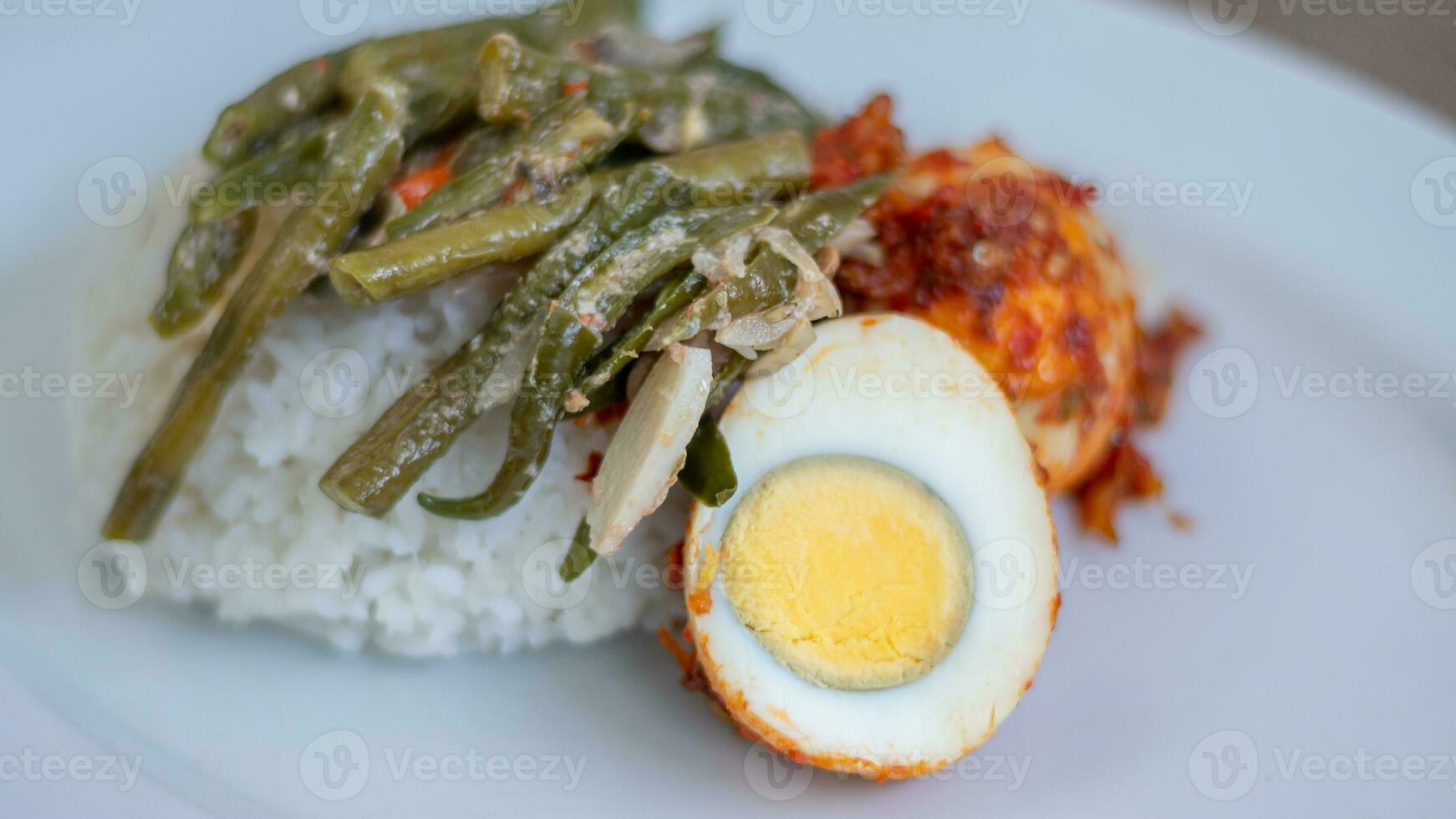 A plate of rice with egg balado and long bean sauce, chili sauce filled with eggs, anchovies and tofu. Served in a bowl on a gray background. Selected focus. photo