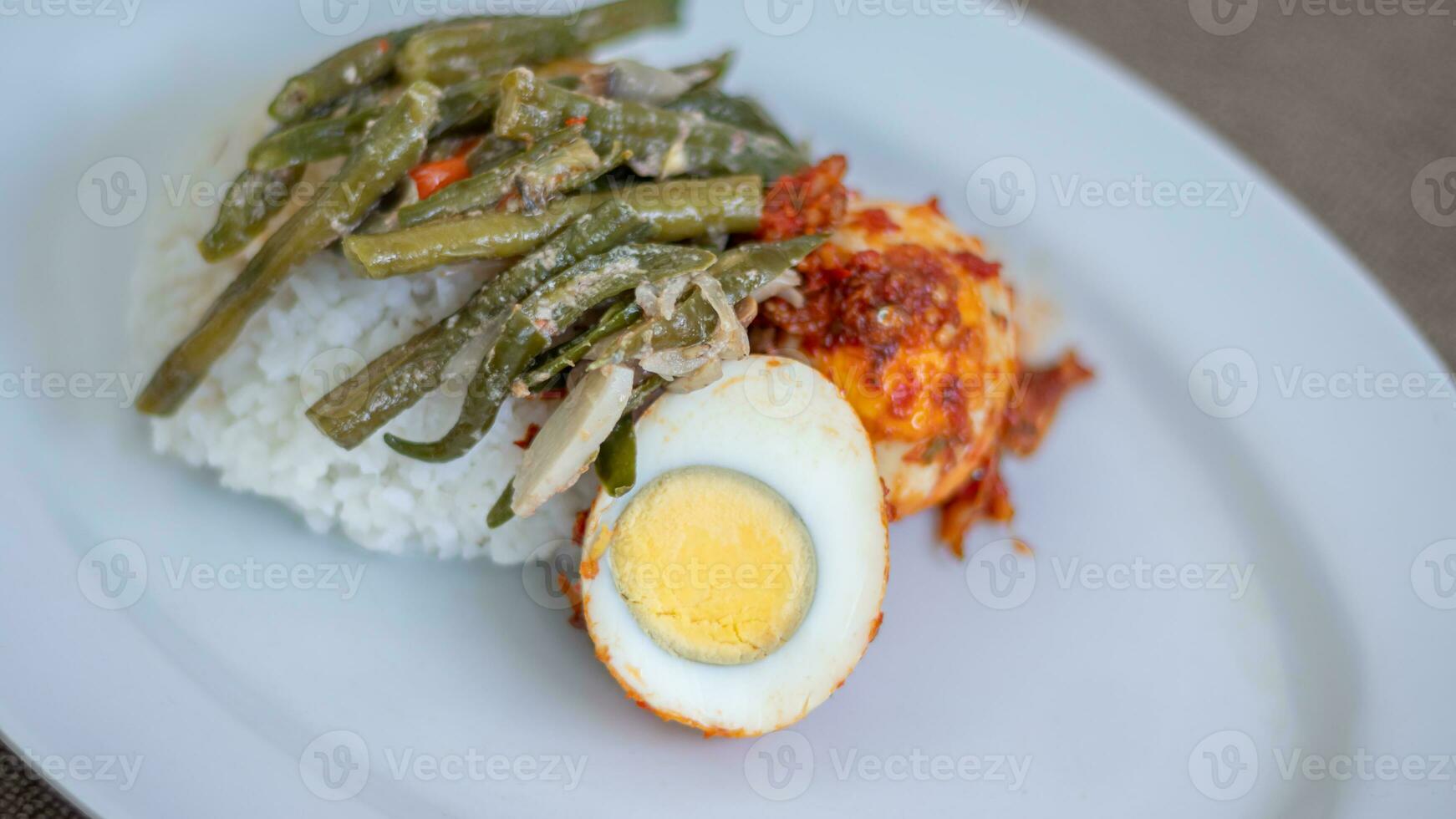 A plate of rice with egg balado and long bean sauce, chili sauce filled with eggs, anchovies and tofu. Served in a bowl on a gray background. Selected focus. photo