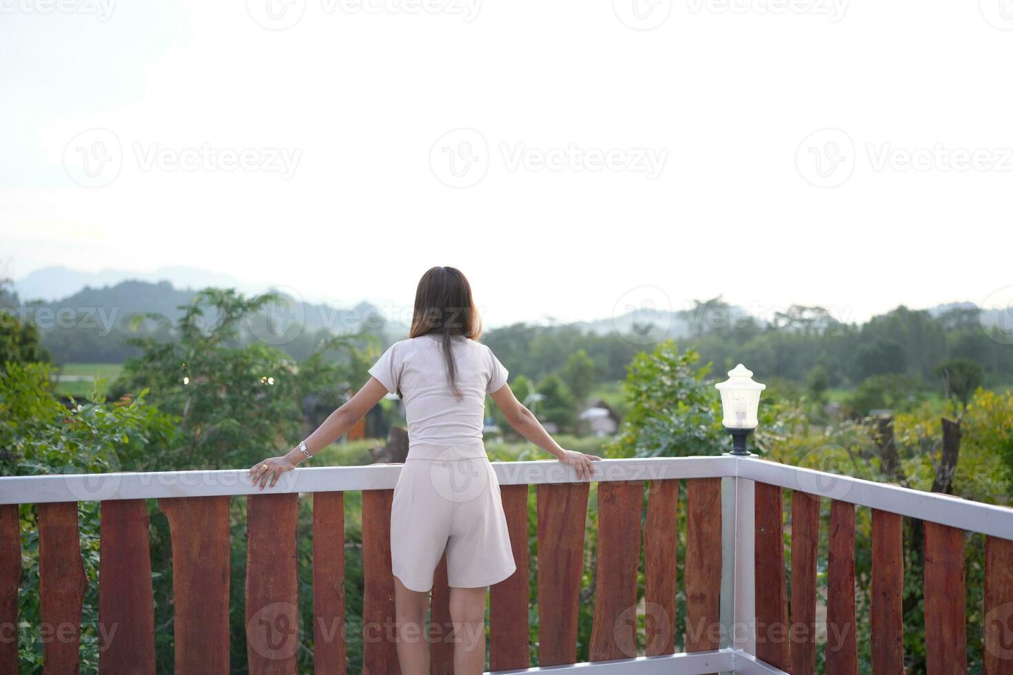 Happy Asian female tourist taking photos on the roof of her accommodation during sunset.