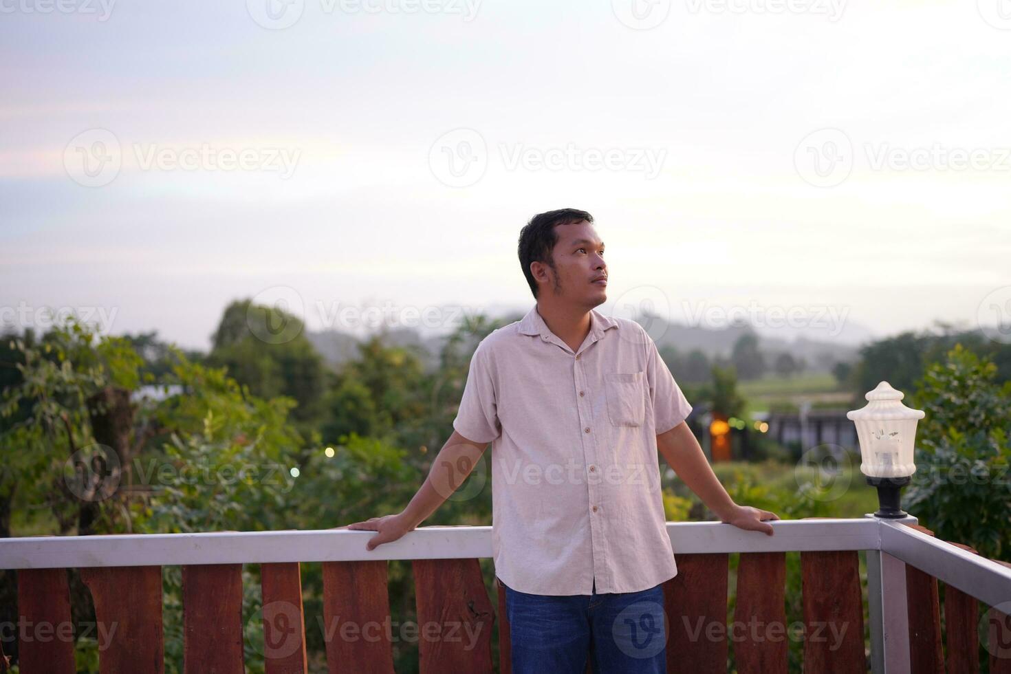 Happy Asian male tourist taking photos on the rooftop of his accommodation during sunset.