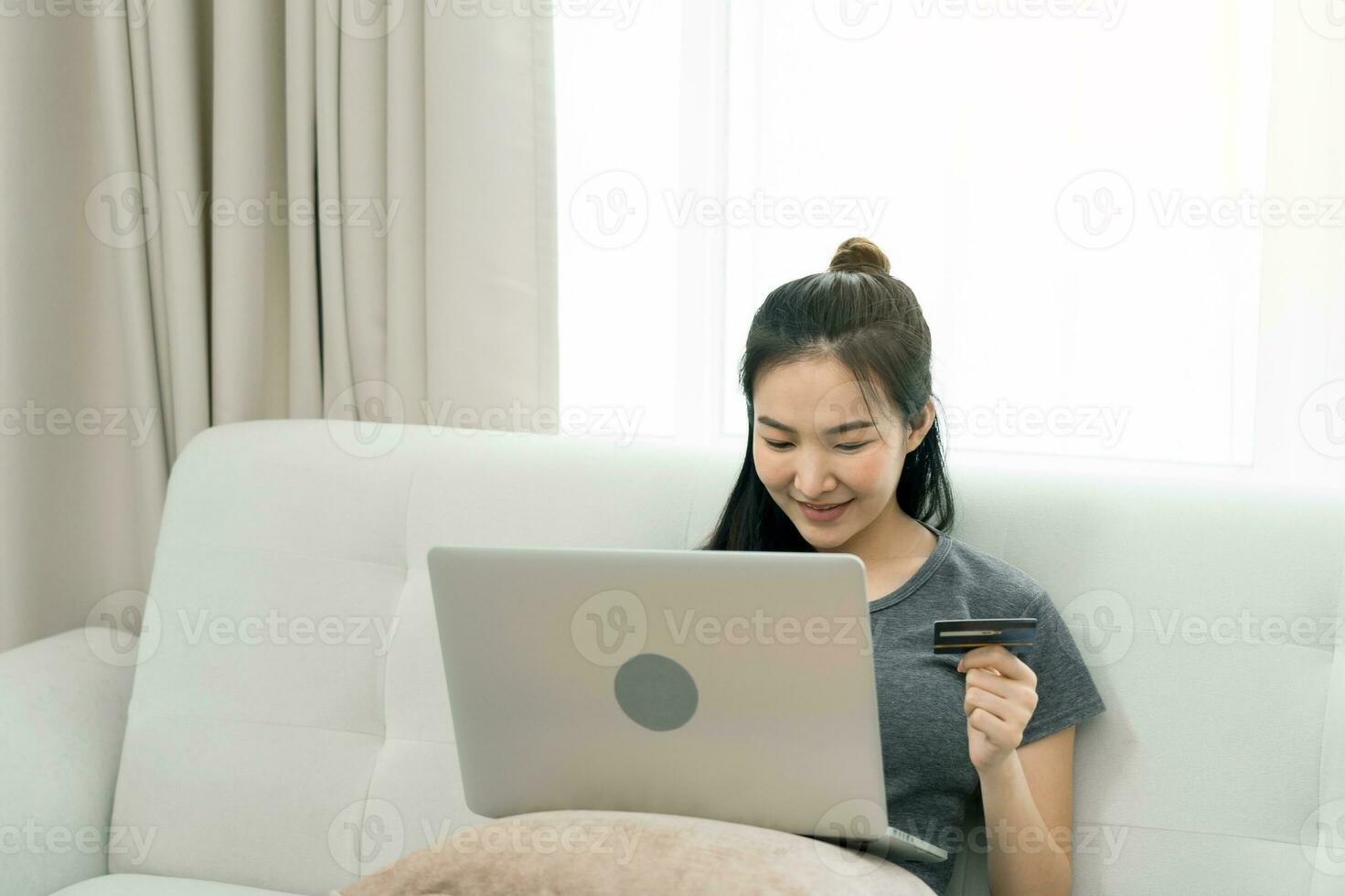 Asian woman holding a credit card for online shopping while sitting on the couch while on vacation at home. photo