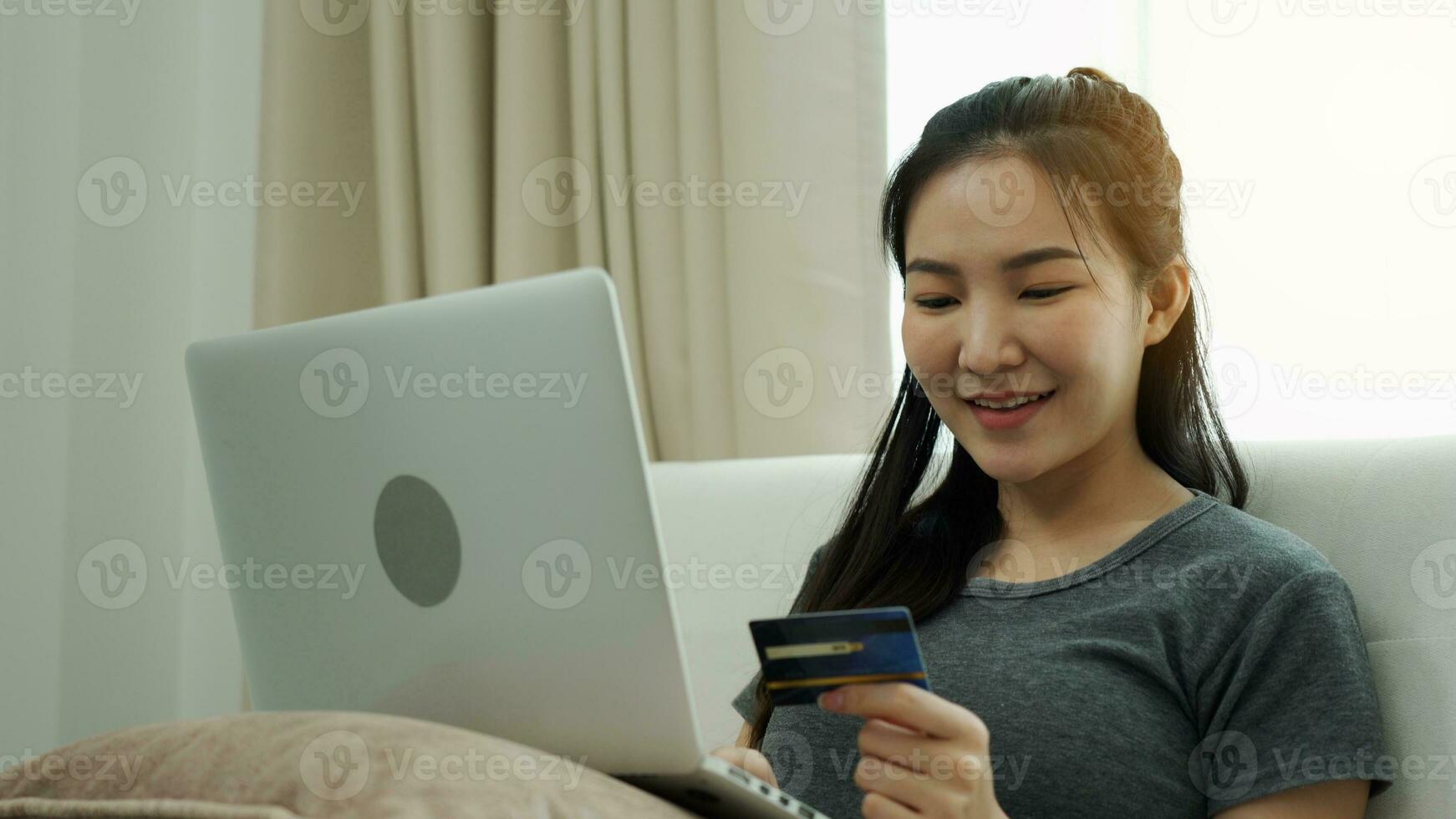 Asian woman holding a credit card for online shopping while sitting on the couch while on vacation at home. photo