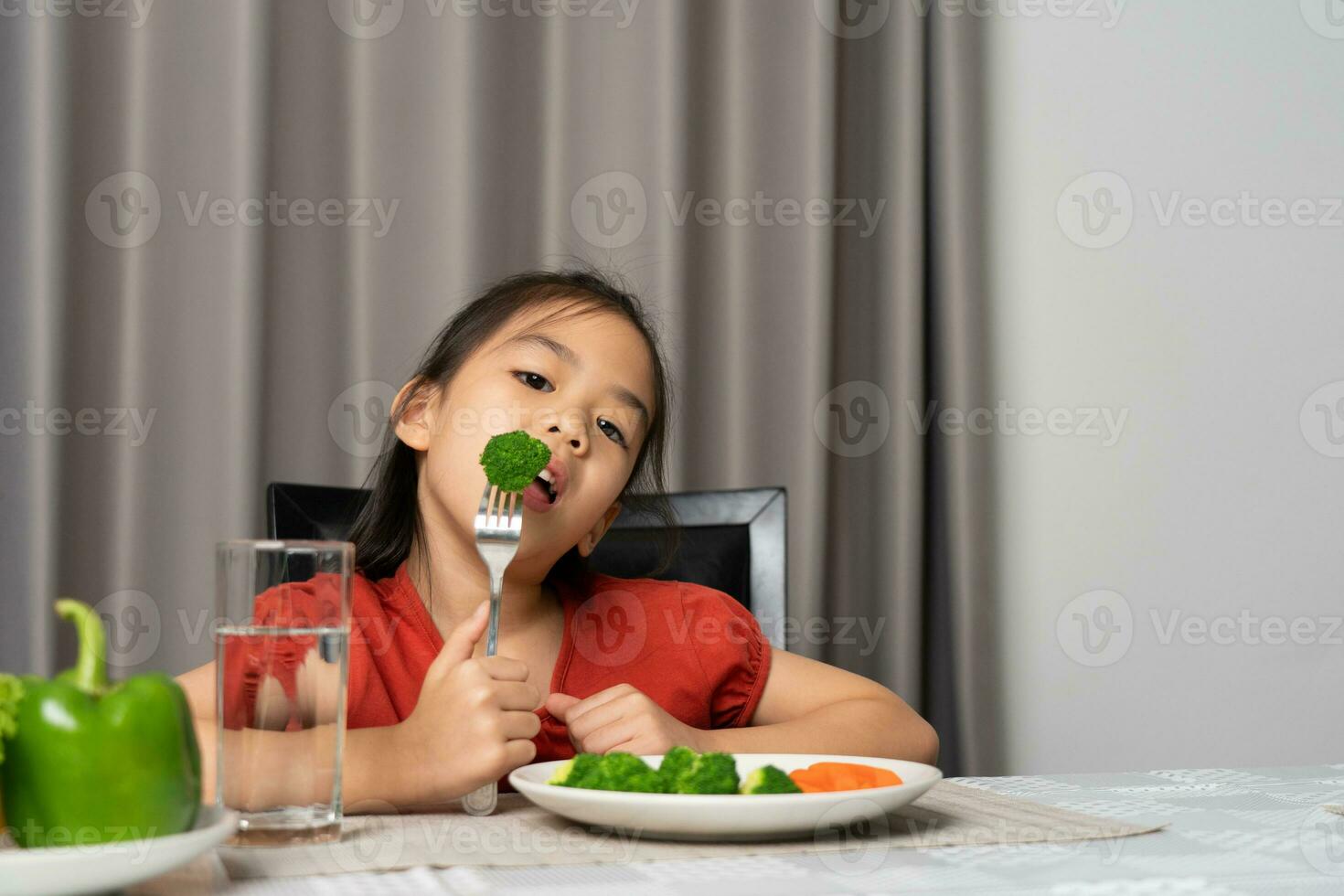 asiático pequeño niña comiendo sano vegetales con saborear. foto