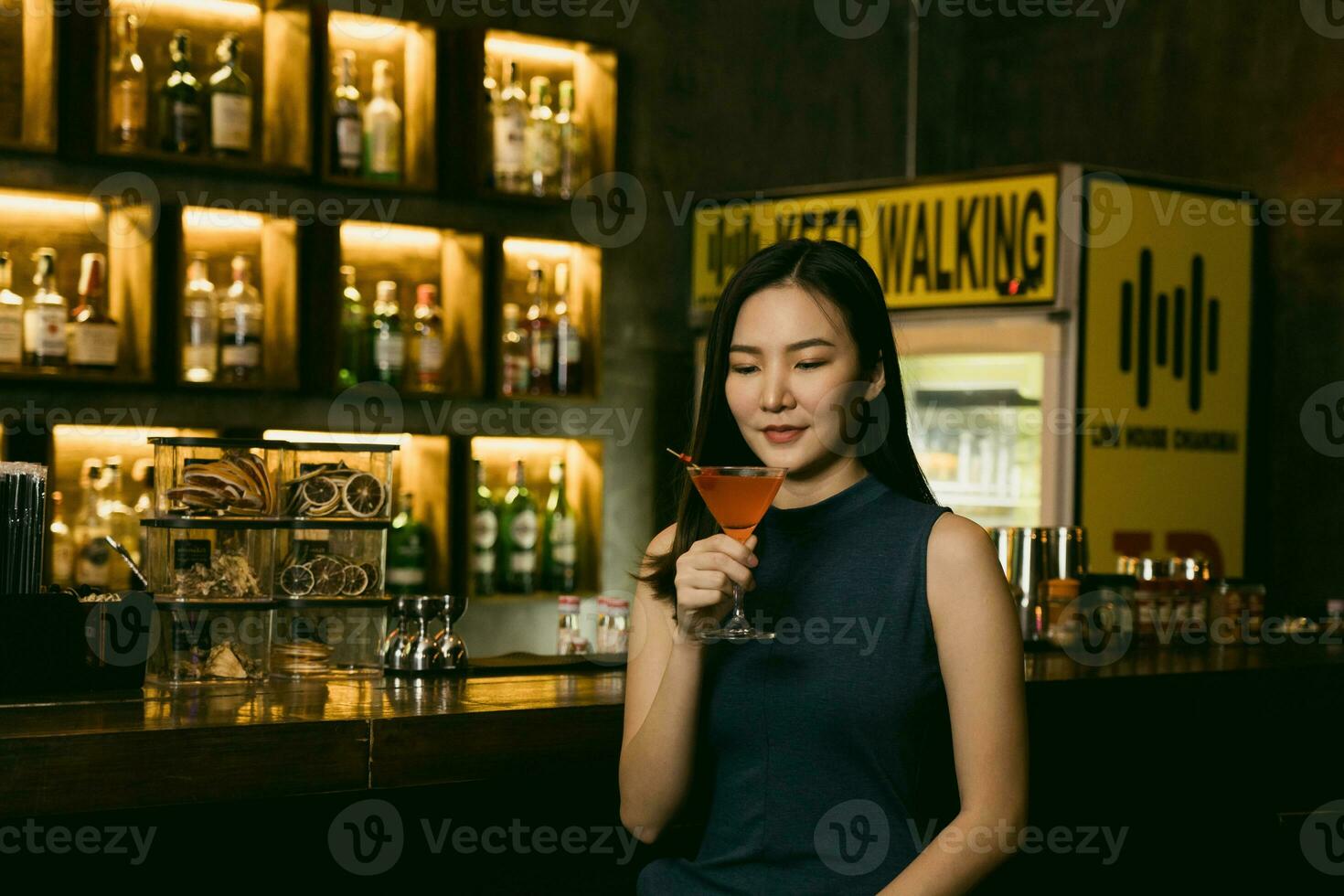 Asian woman drinking a cocktail at a bar at night. photo