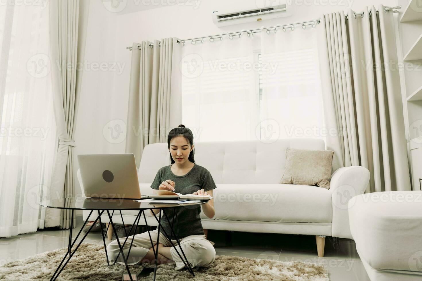 una joven asiática se sienta en la sala de estar usando una calculadora para calcular los ingresos y gastos familiares y lo escribe en su cuaderno o computadora portátil en casa. foto