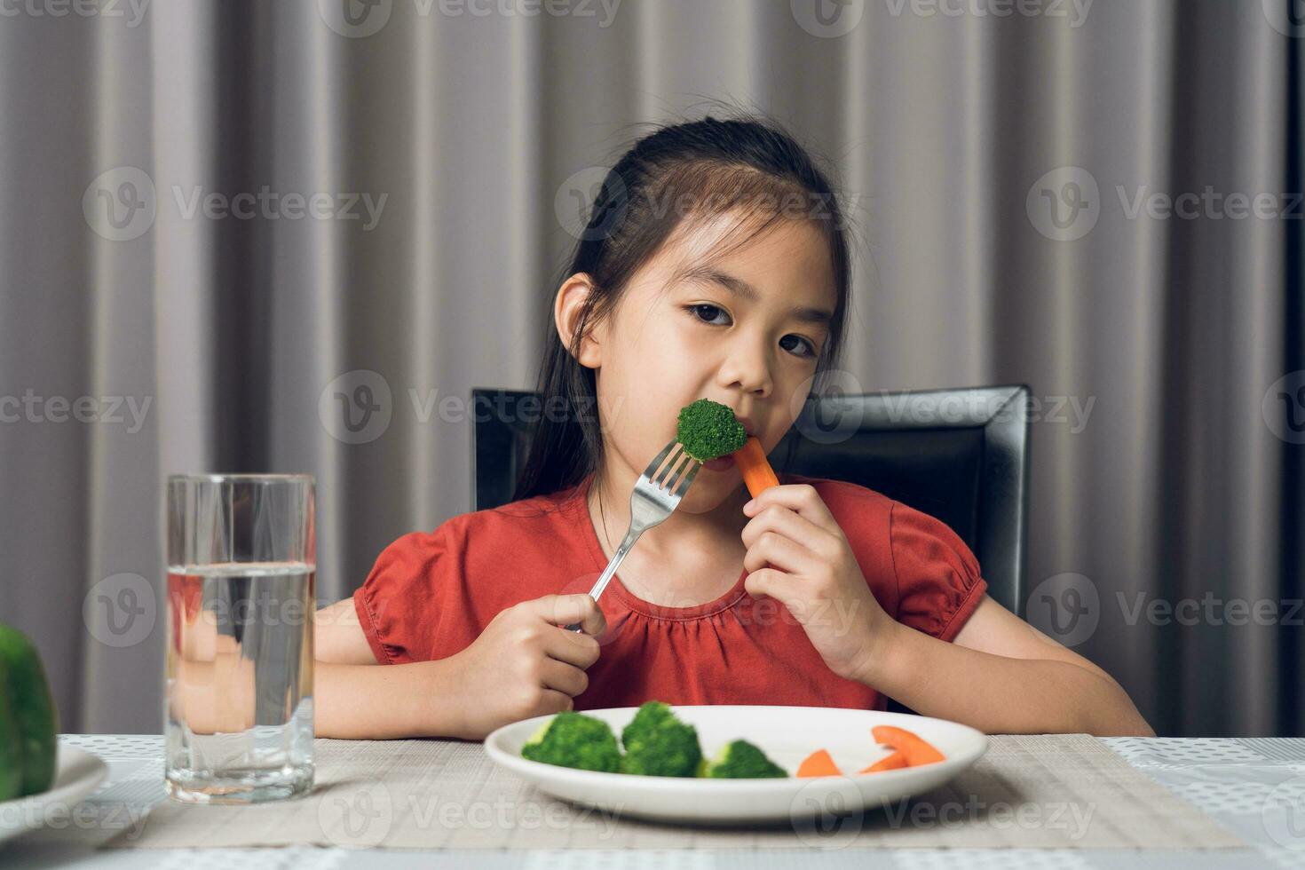 Asian little girl eating healthy vegetables with relish. photo