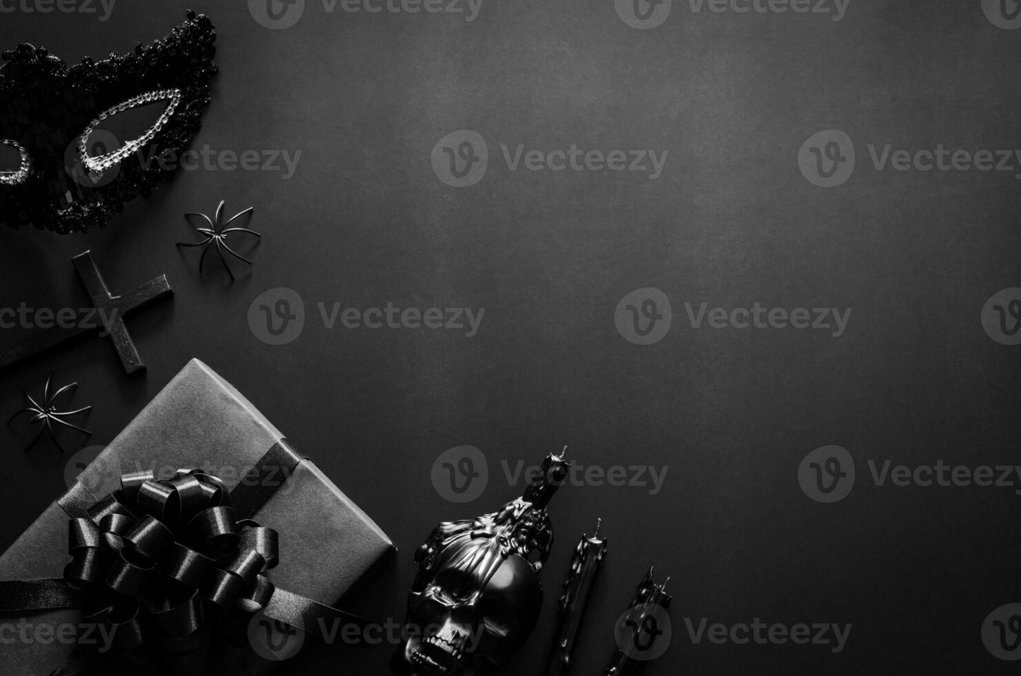 Víspera de Todos los Santos fiesta concepto con negro accesorios, regalo caja, lujoso mascarilla, el cruzar y cráneo vela en negro antecedentes. foto