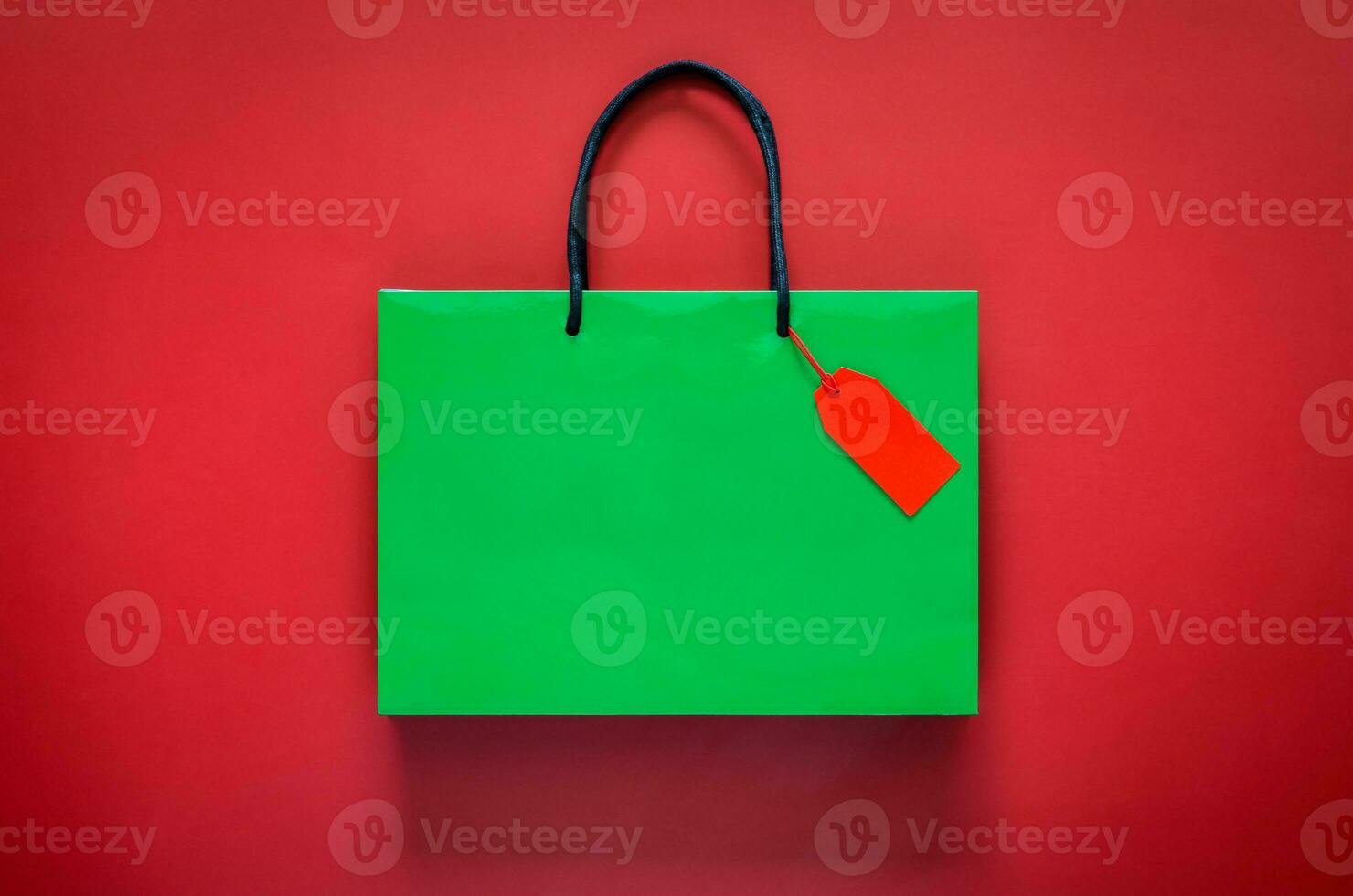 Green shopping paper bag with red blank price tag on red background for Black Friday shopping sale concept. photo