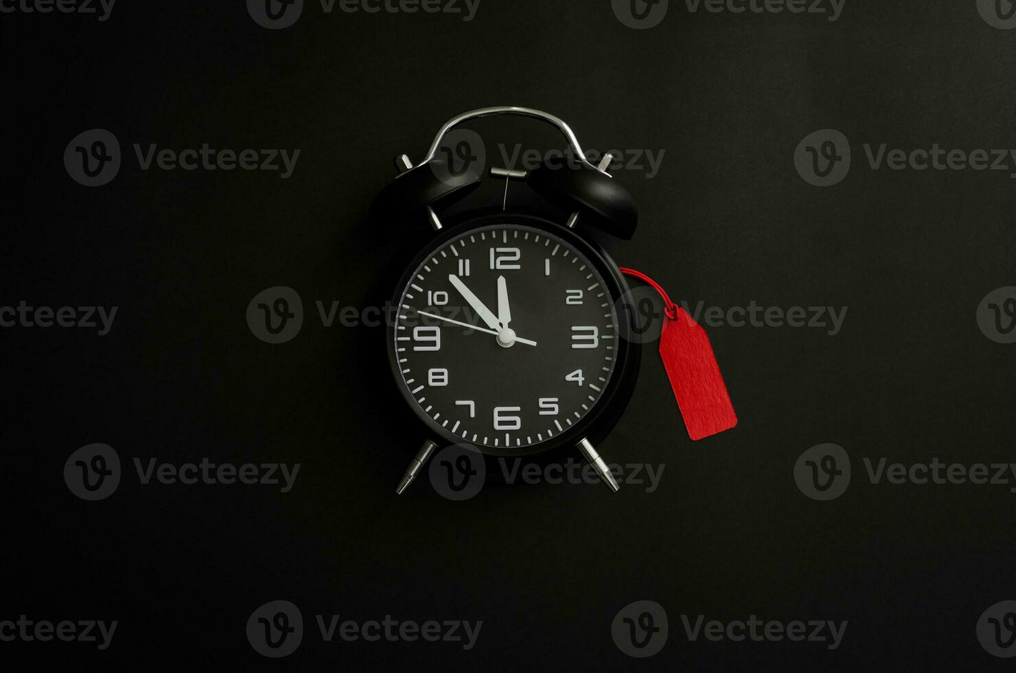 Black alarm clock with red blank price tag on black background for Black Friday shopping sale concept. photo