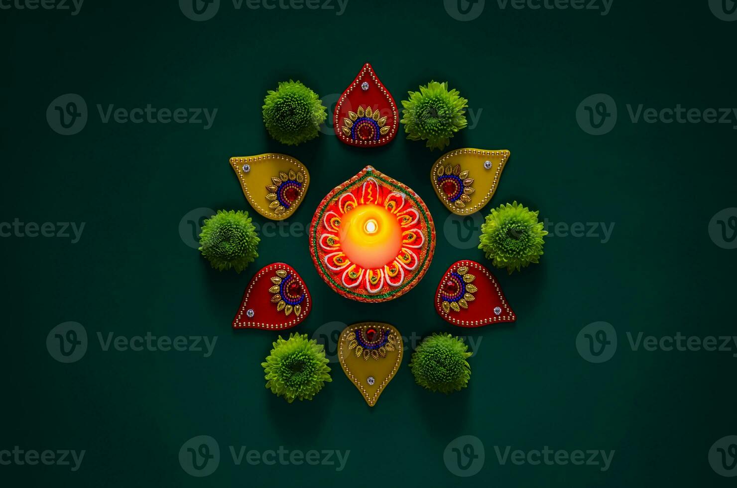 Clay diya lamp lits to celebrate for Diwali festival with colorful decoration objects and green flowers on dark green background. photo