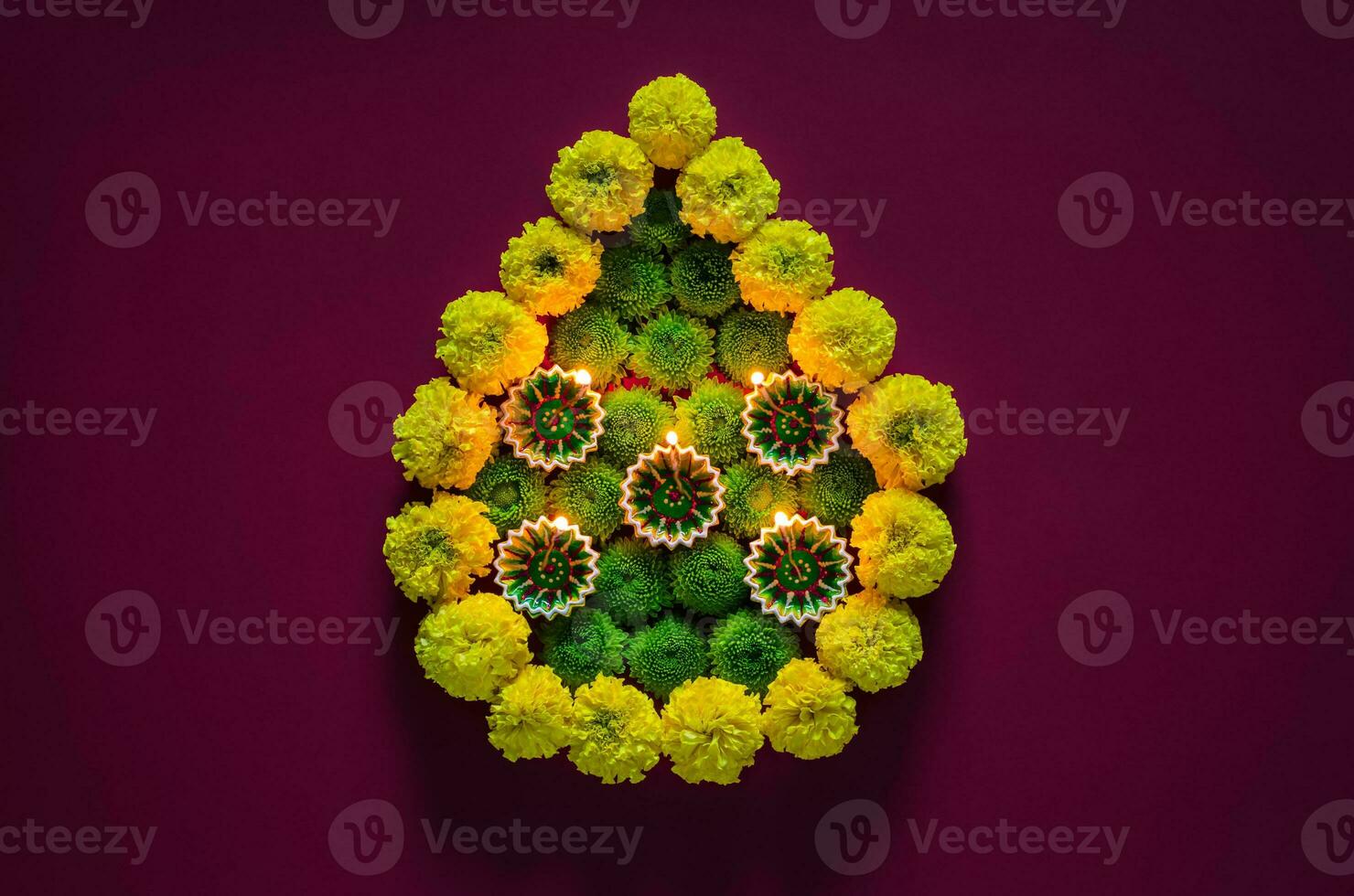 Clay diya lamps lit to celebrate for Diwali festival with colorful flowers set as flame shape on dark purple background. photo