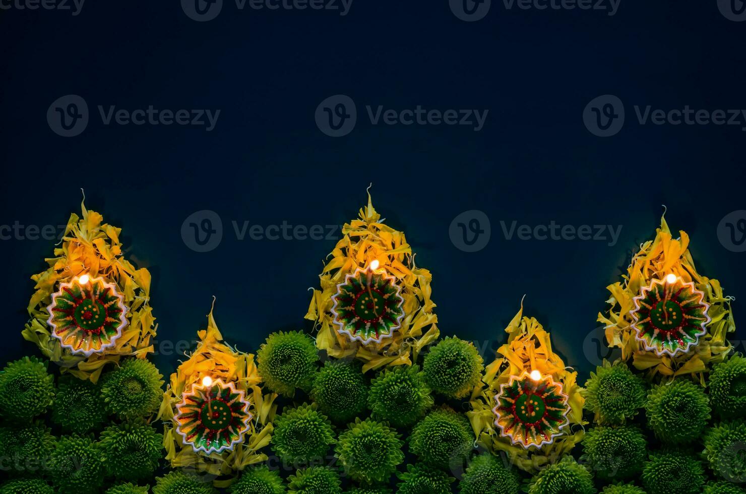 arcilla diya lamparas conjunto como fuego forma iluminado a celebrar para diwali festival con vistoso flores en oscuro azul antecedentes. foto